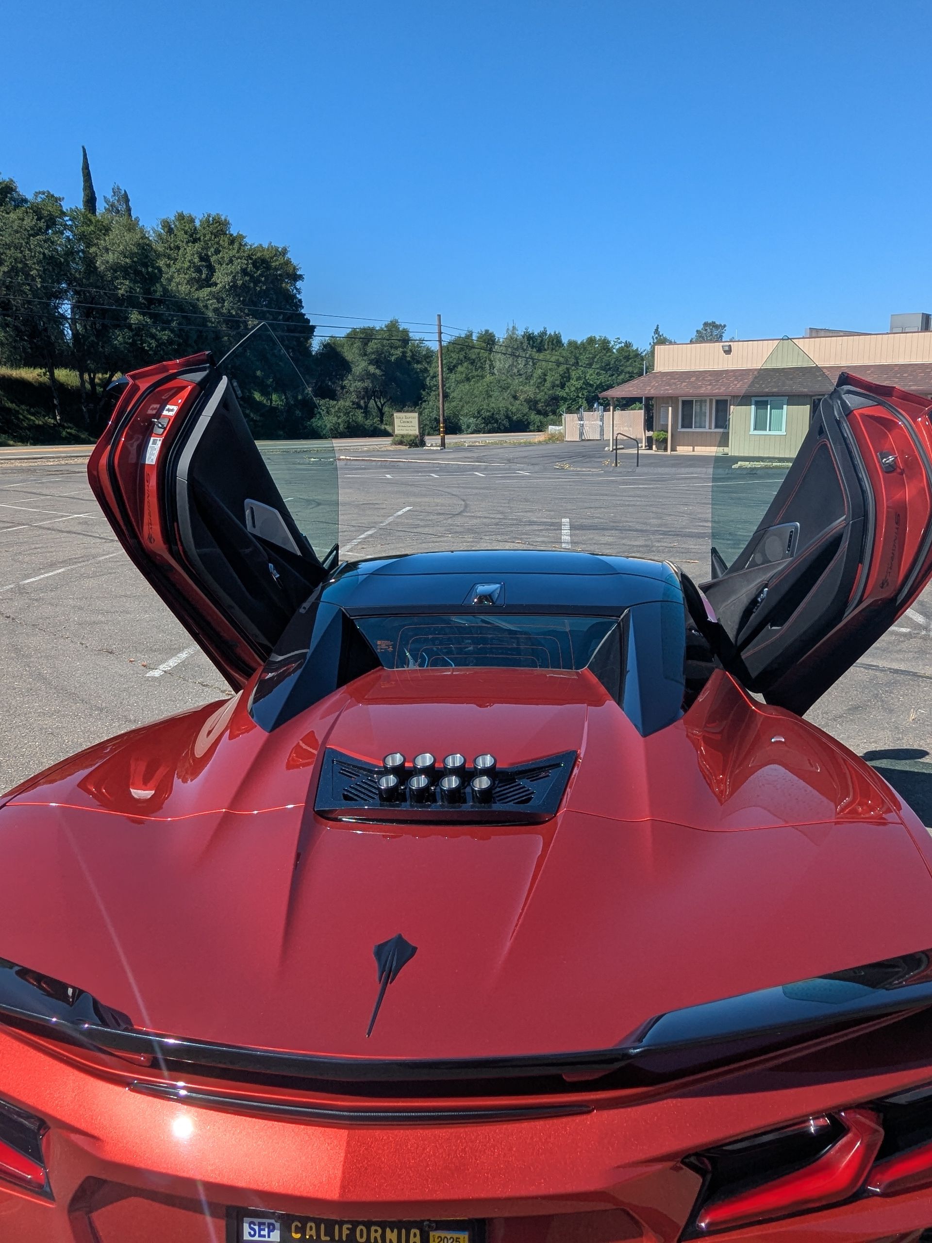 Red sports car with its doors open is parked in a parking lot