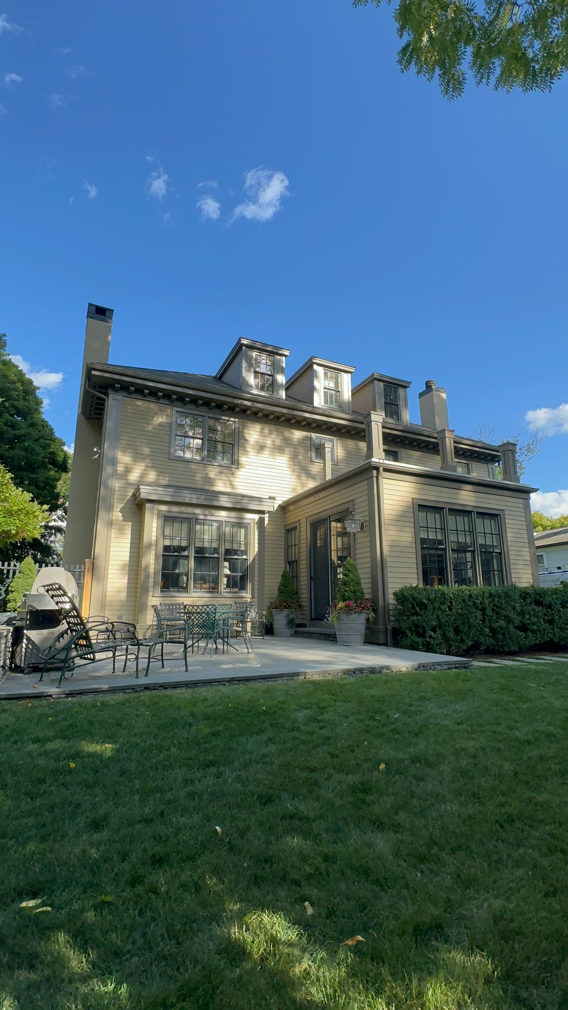 Beige stucco house with a slate roof, a grassy yard, and blue sky.