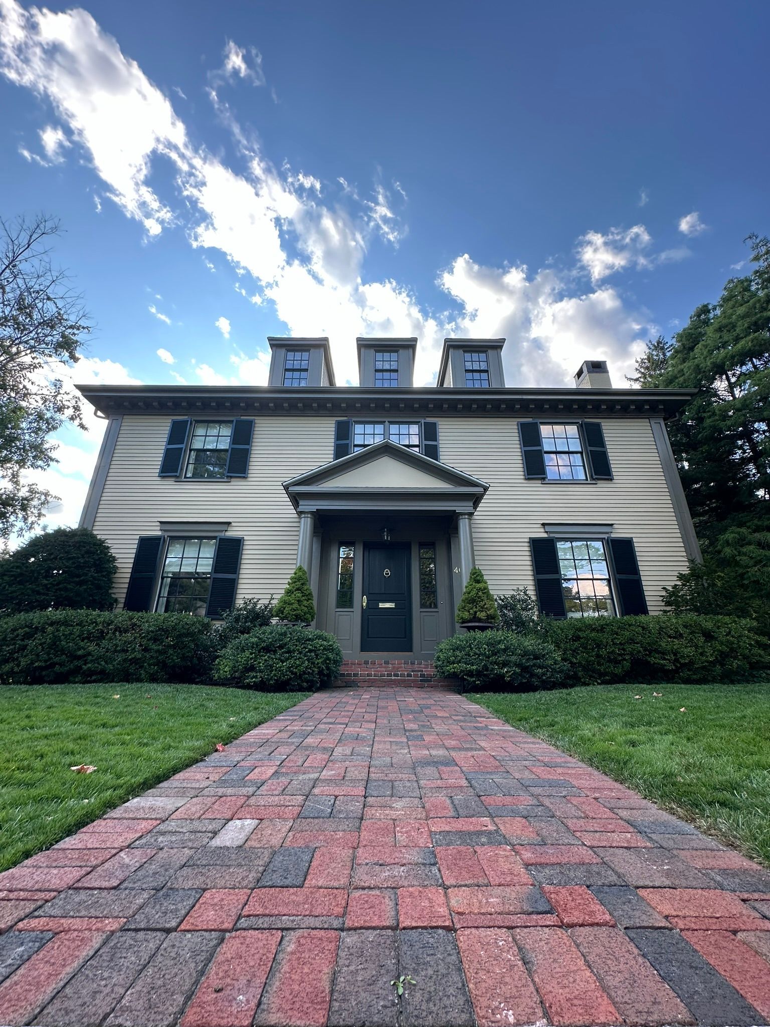 Two-story house with green door, shutters, and brick walkway under a blue sky.