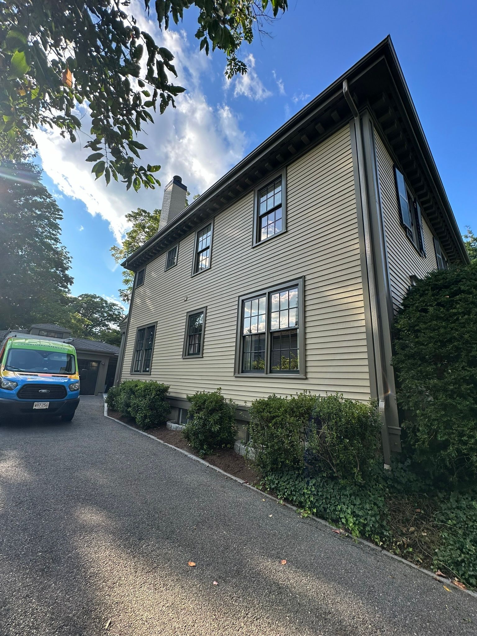 A two-story house with unique swirling pattern on the siding, gravel driveway, and a van.