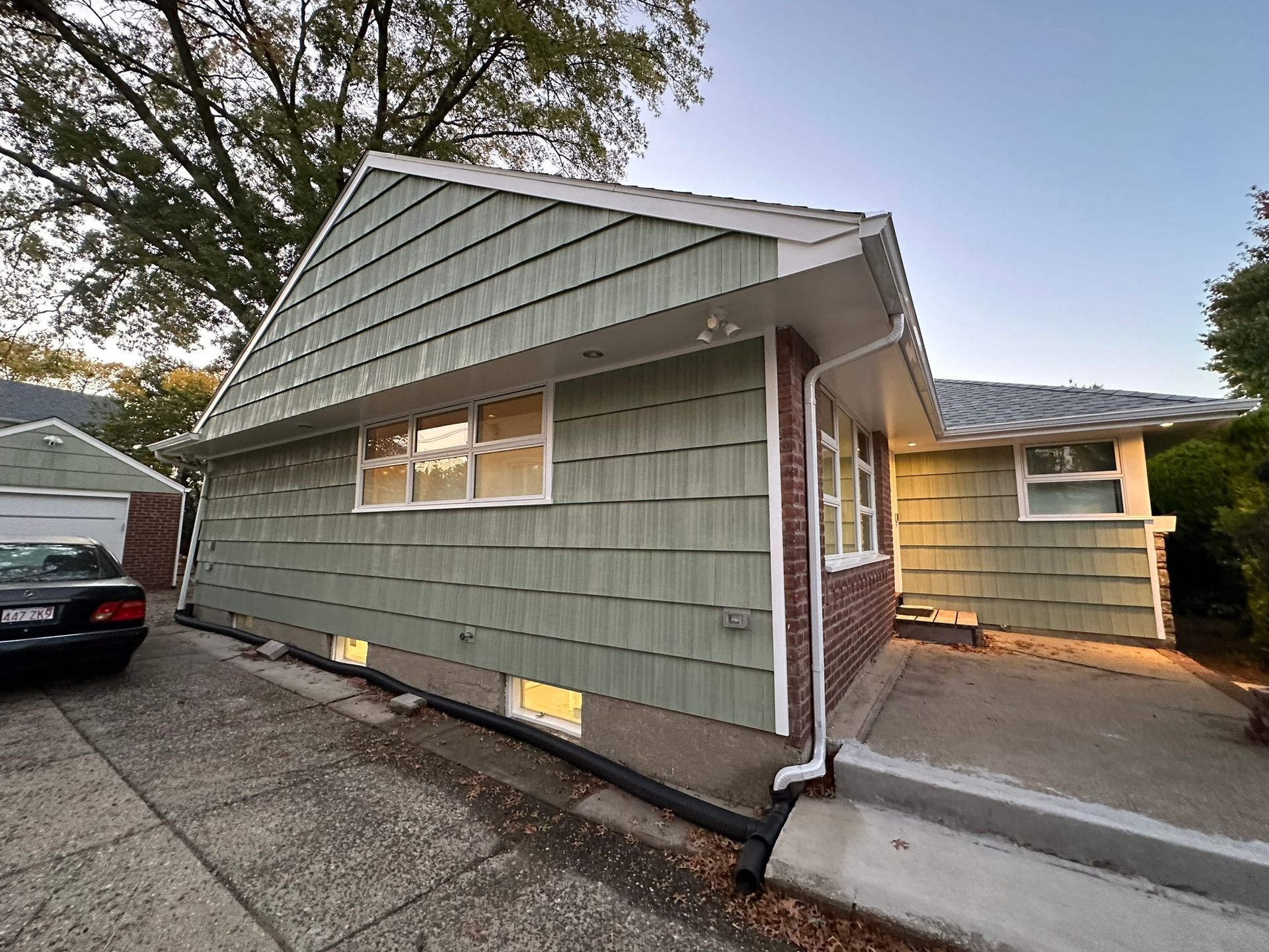 A house with green siding, a brick facade, and a driveway.
