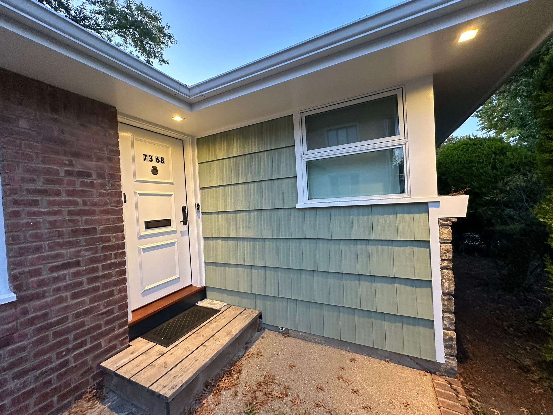 Exterior of a house entrance with a white door, light green siding, and a wooden step.