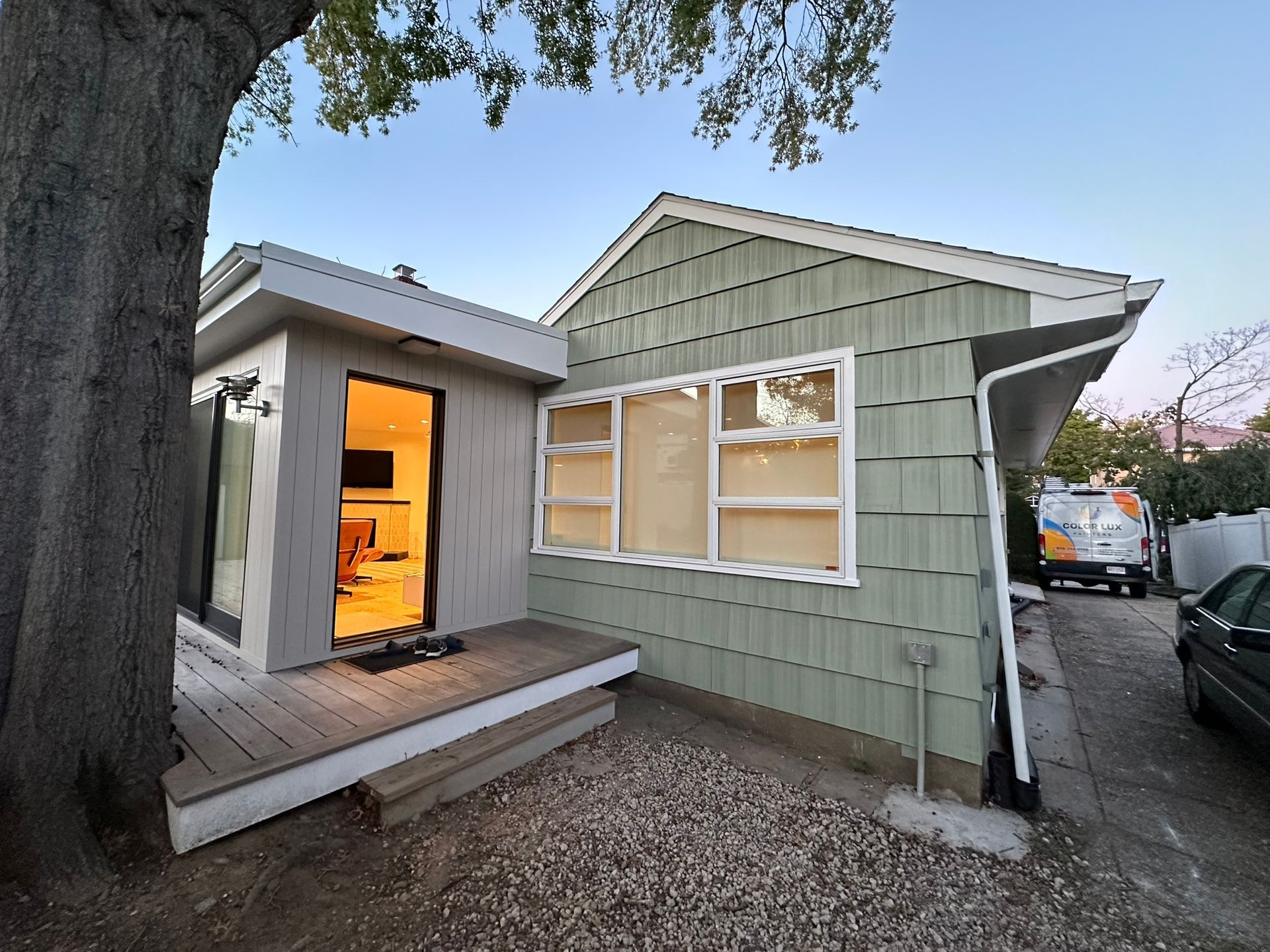 Small house with green siding, open door, porch, and a tree. Evening light.