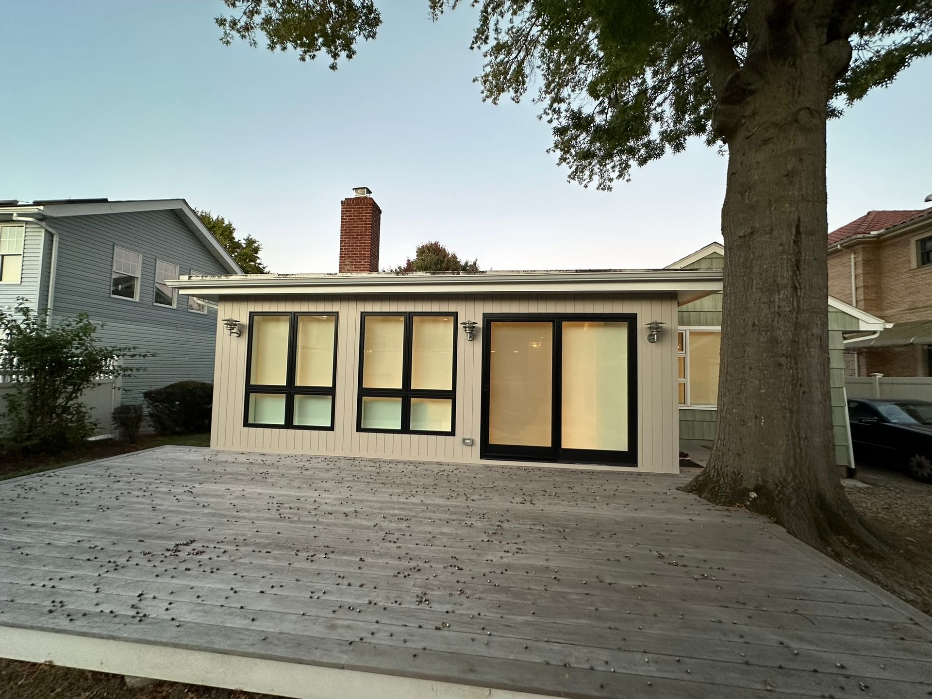 Exterior of a light-colored building with large windows and a concrete patio. A large tree is to the right.