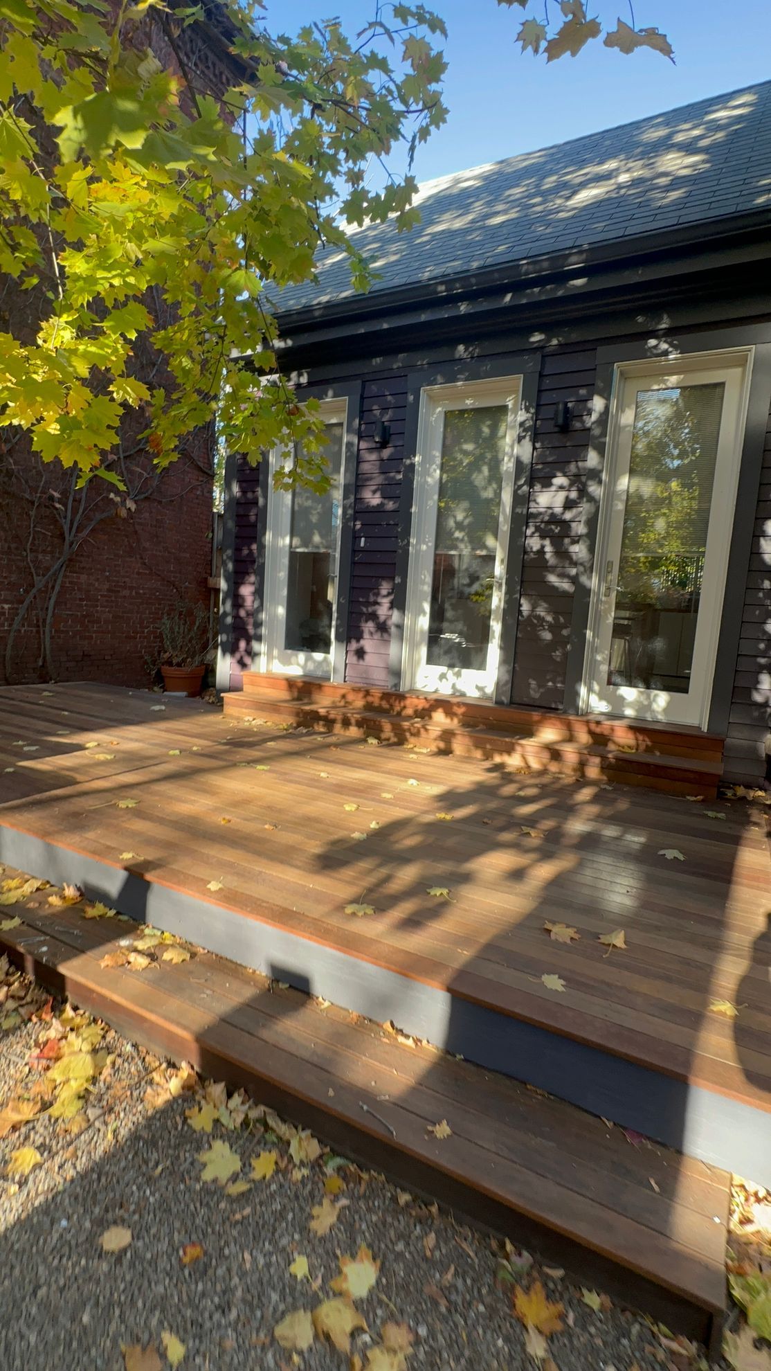 Wooden deck with steps in front of a black building with tall windows; autumn leaves scattered.