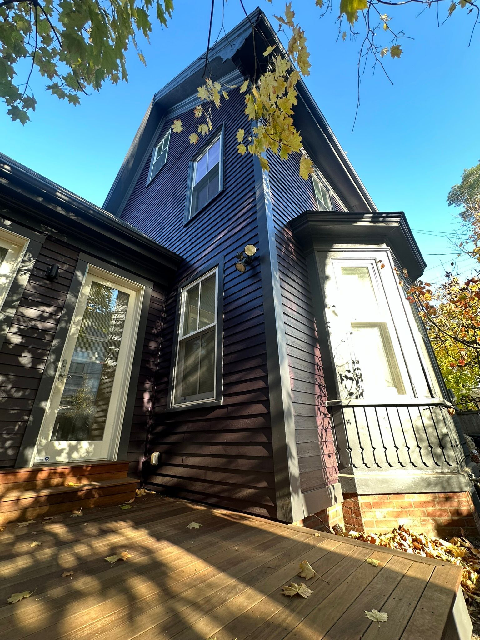 Dark wood-paneled house with white window frames and a small porch on a sunny day.