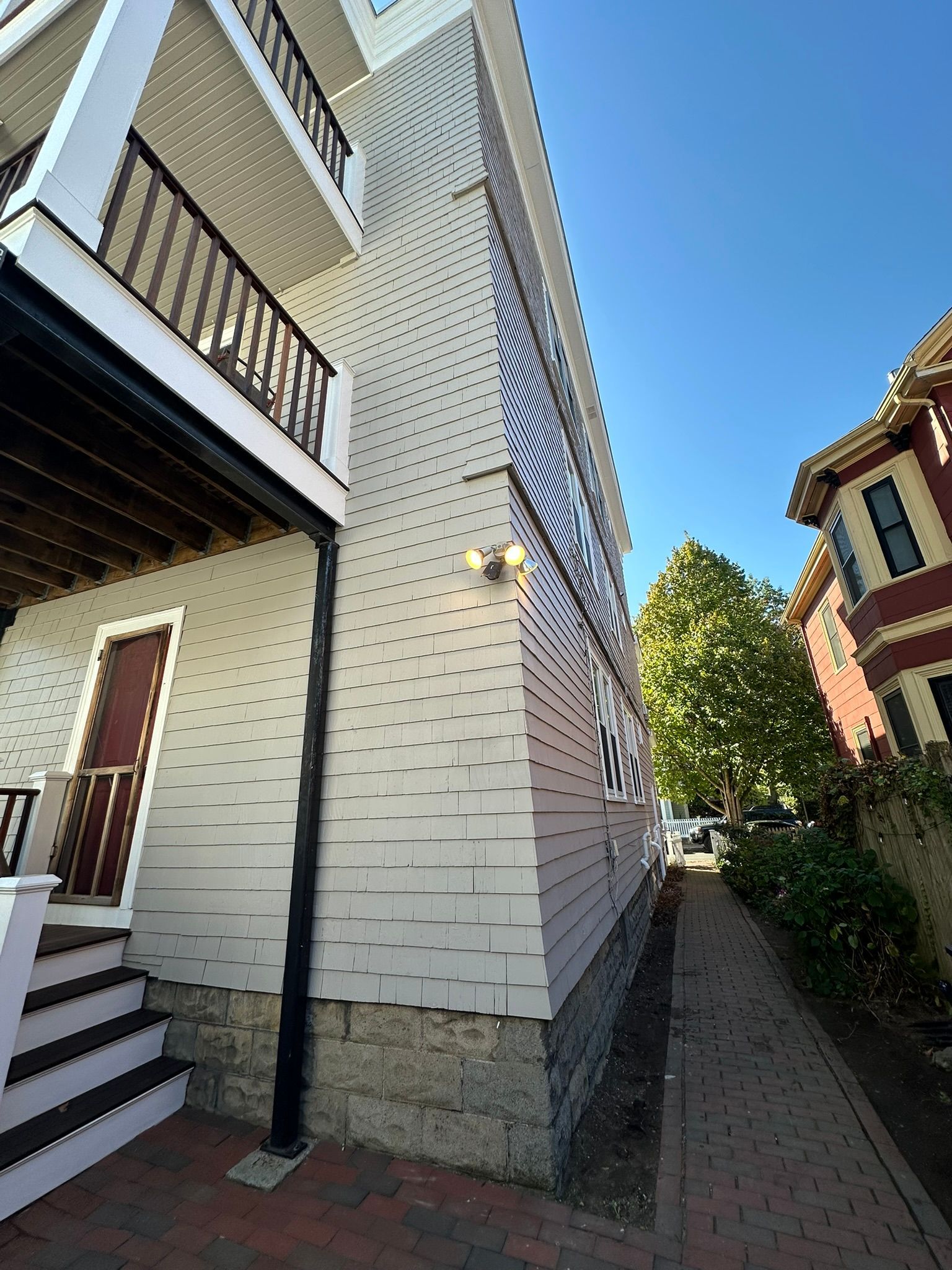 Side view of a light-colored building with a narrow brick walkway and blue sky.