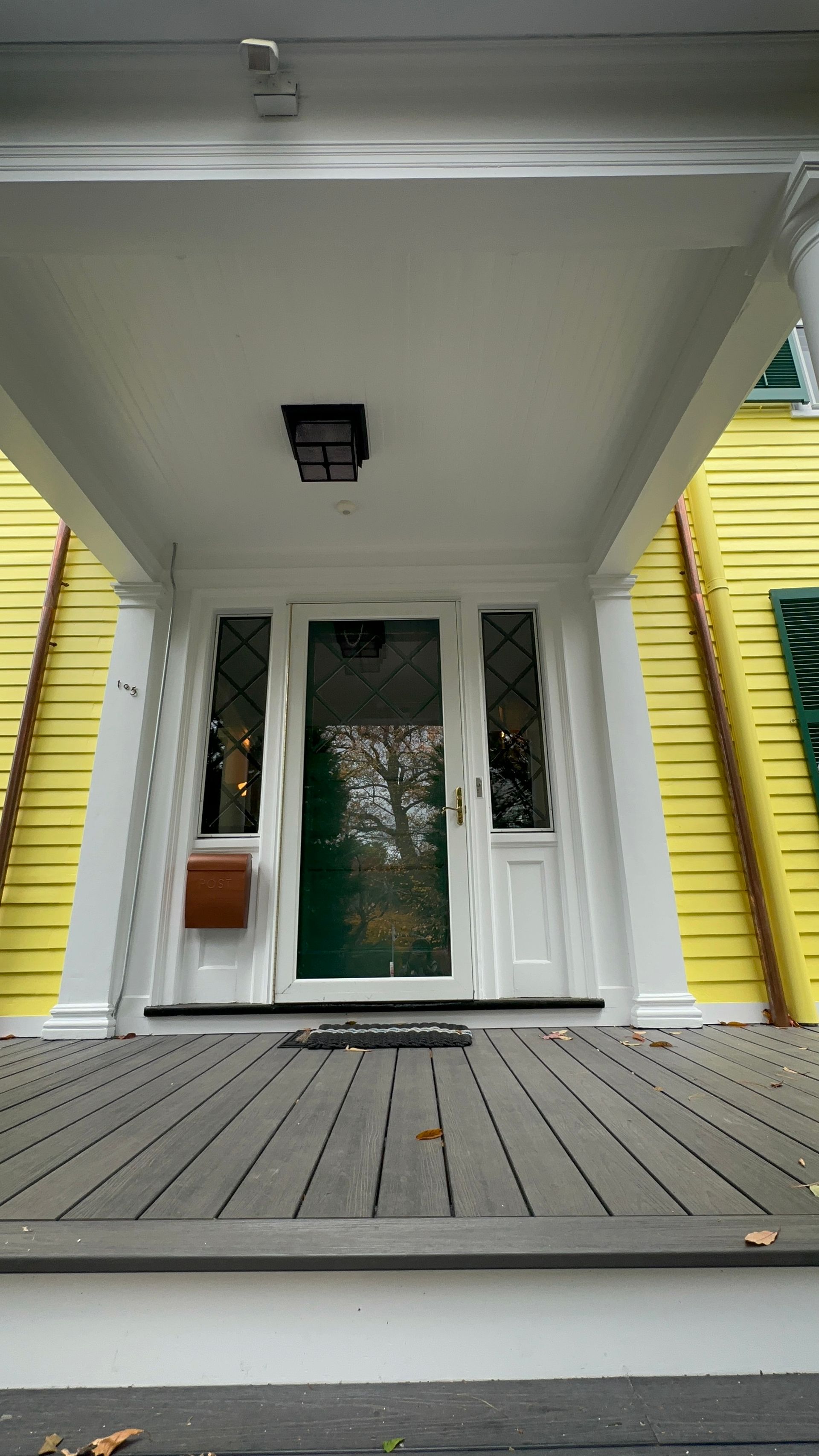 Yellow house with white porch and door, view from the porch steps, overhead light.