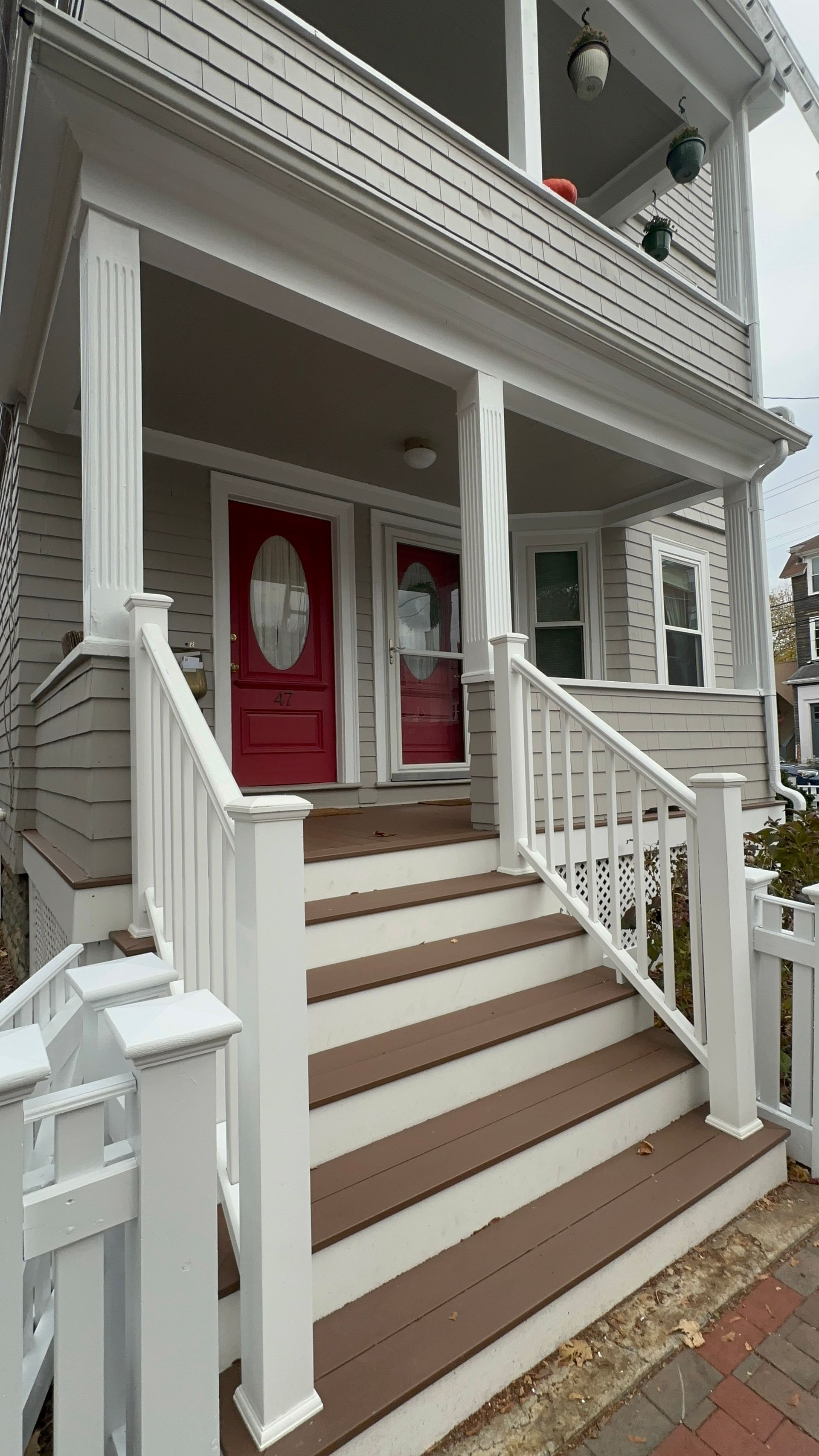 White porch with red doors, stairs, and gray siding.
