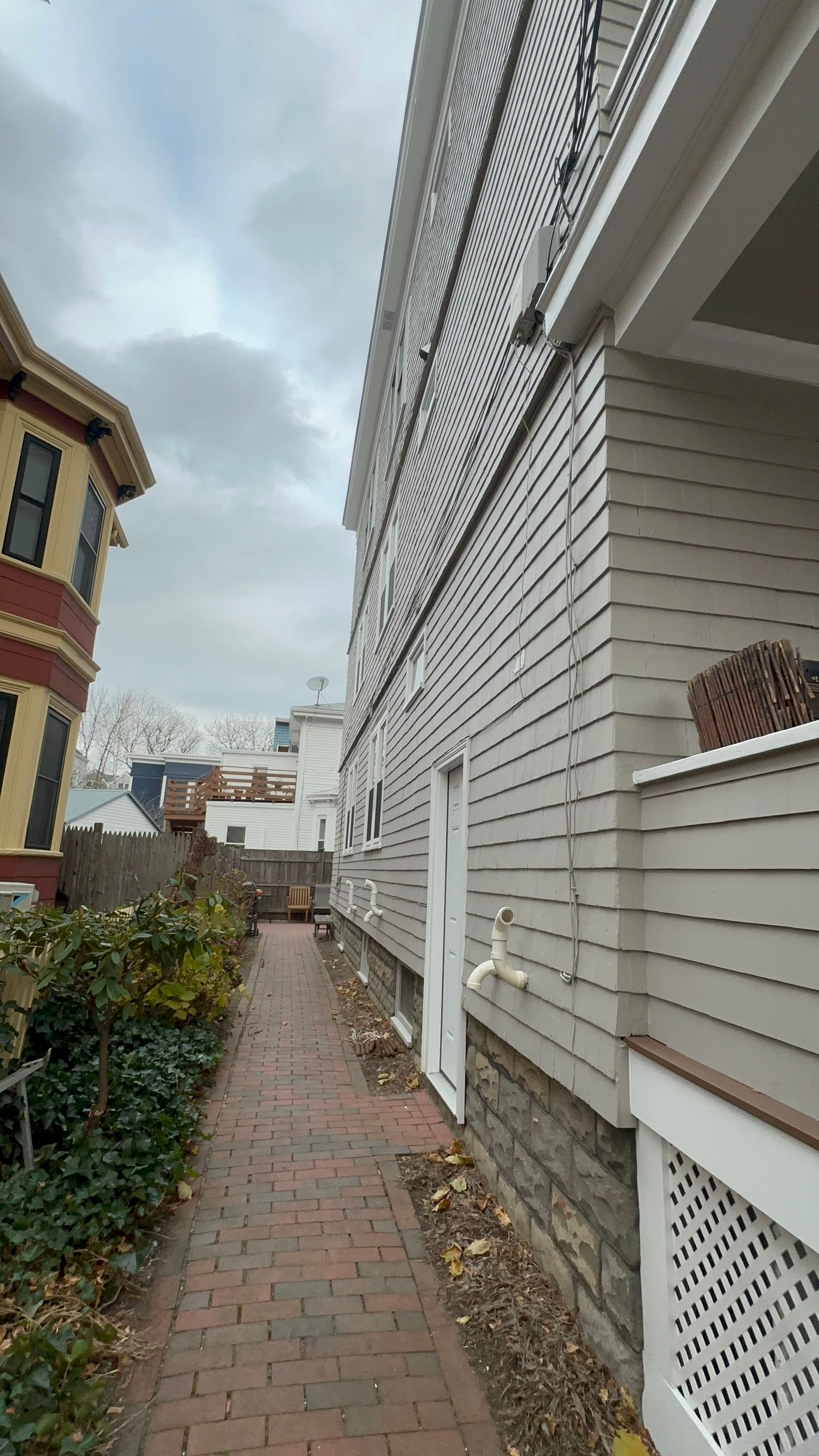 Brick path between buildings, gray siding, white door, and cloudy sky.