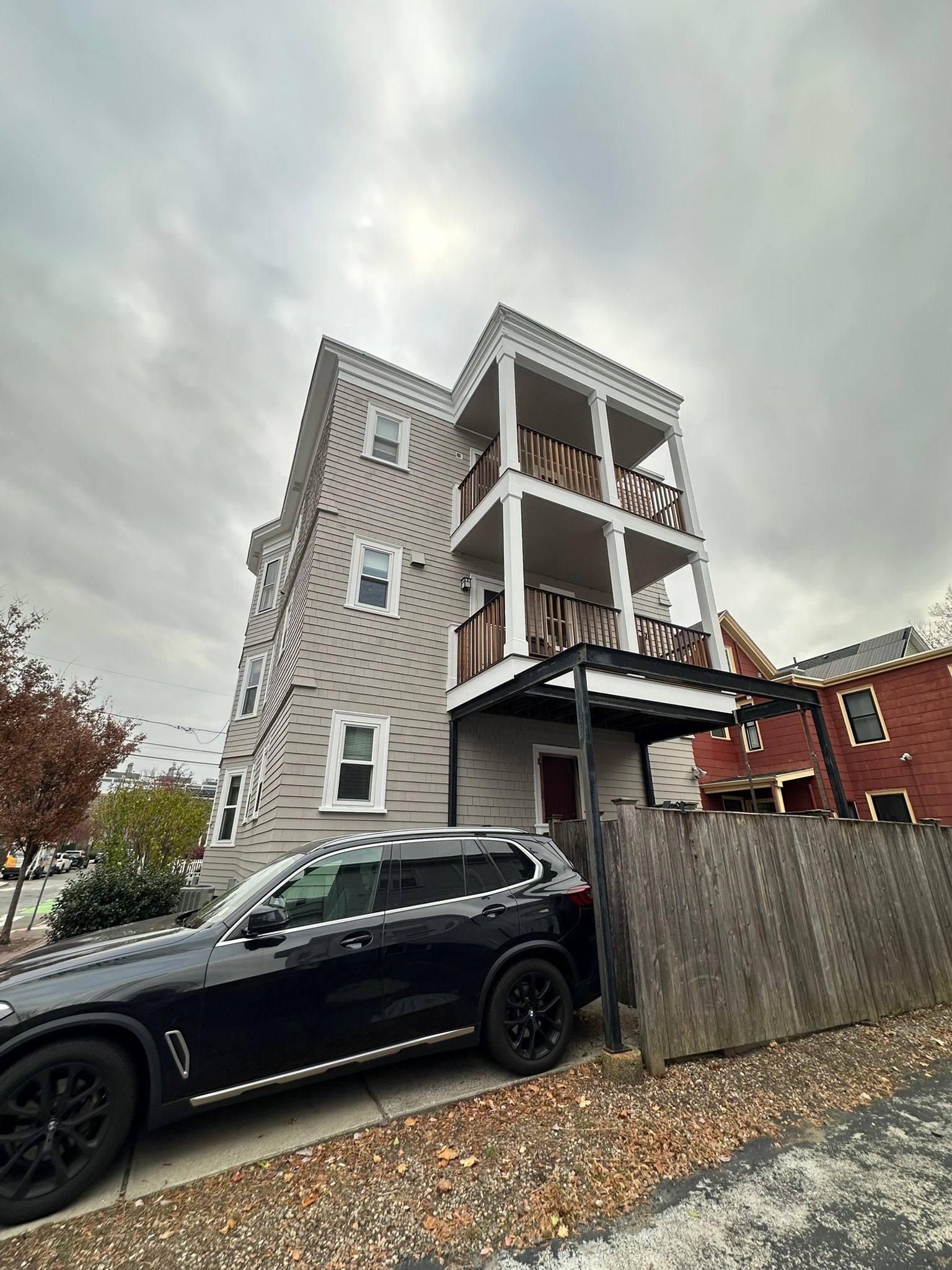 Multi-story gray house with balconies, black SUV parked in front on a cloudy day.