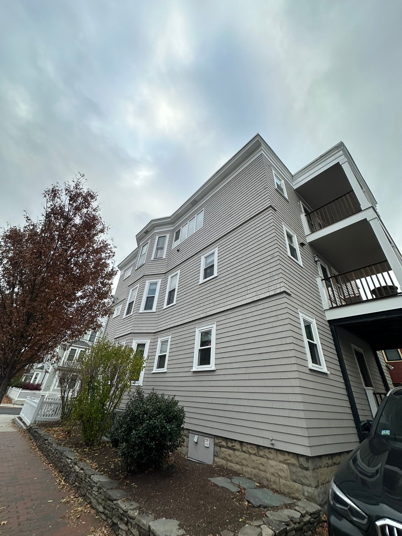 Gray multi-story building with balconies under a cloudy sky.