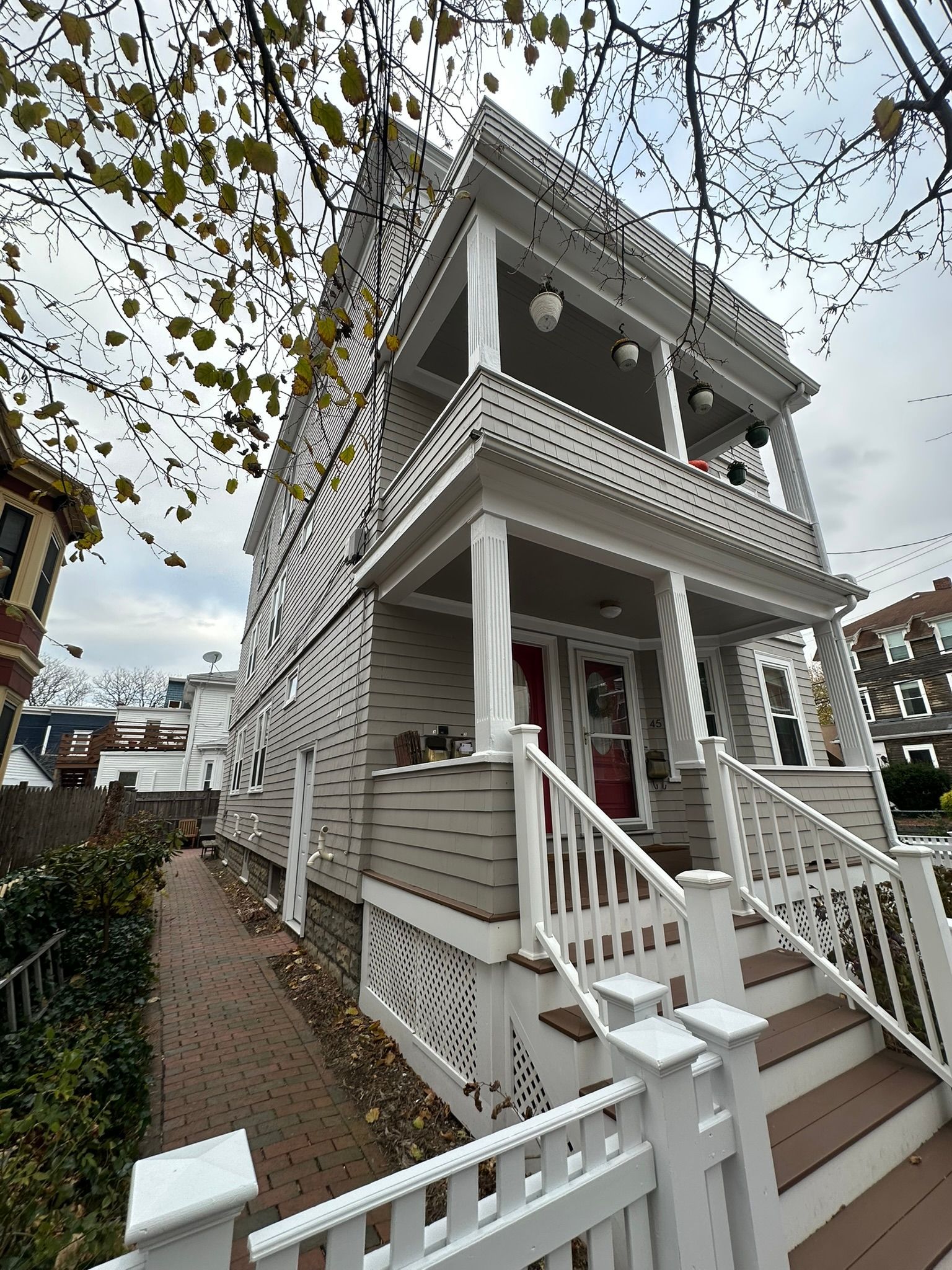 Three-story house with white trim, multiple porches, and a brick walkway on a cloudy day.