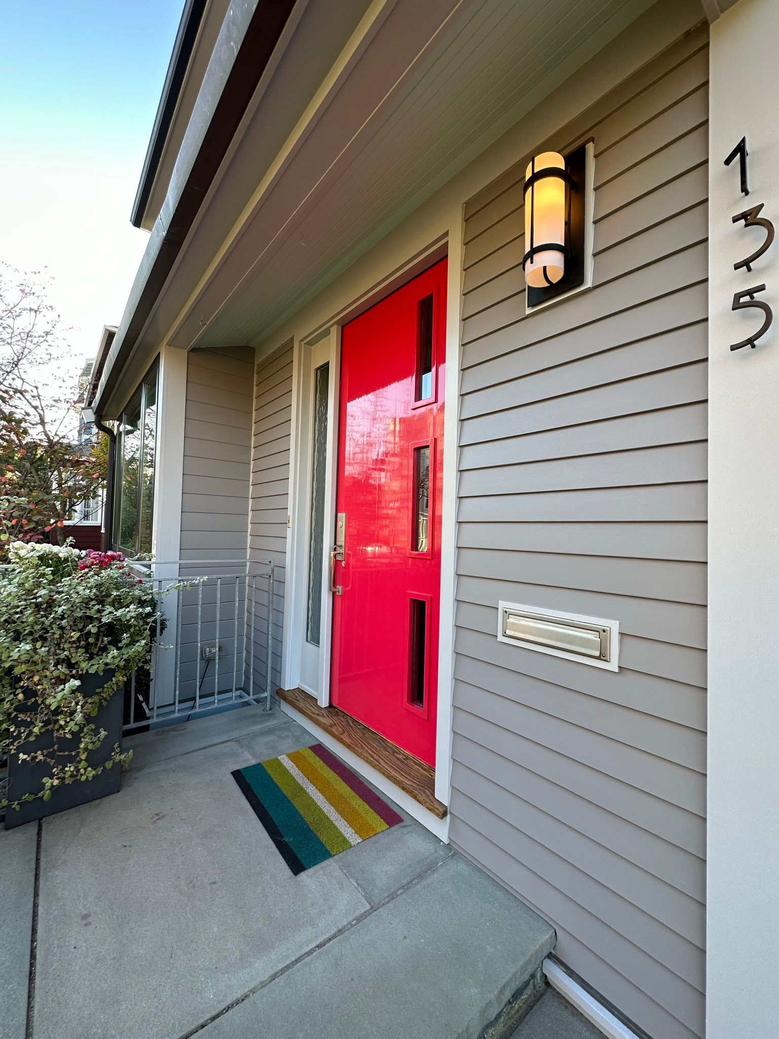 Bright red front door with sidelights, under a gray overhang.  Address numbers 