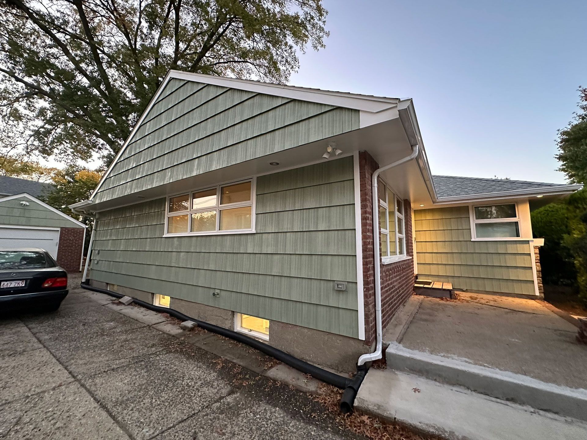 A light green-sided house with white trim, a concrete driveway, and a black car parked beside it.