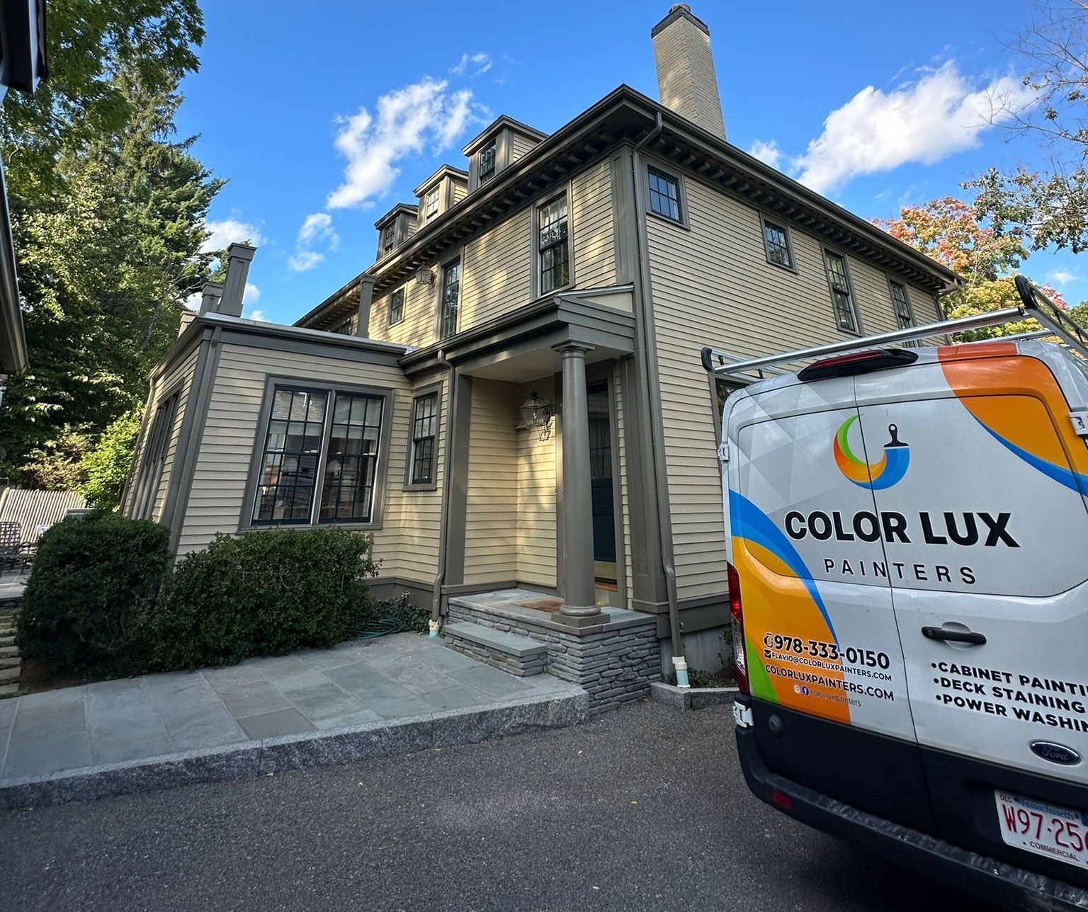 A house with tan siding and a Color Lux Painters van parked in front.