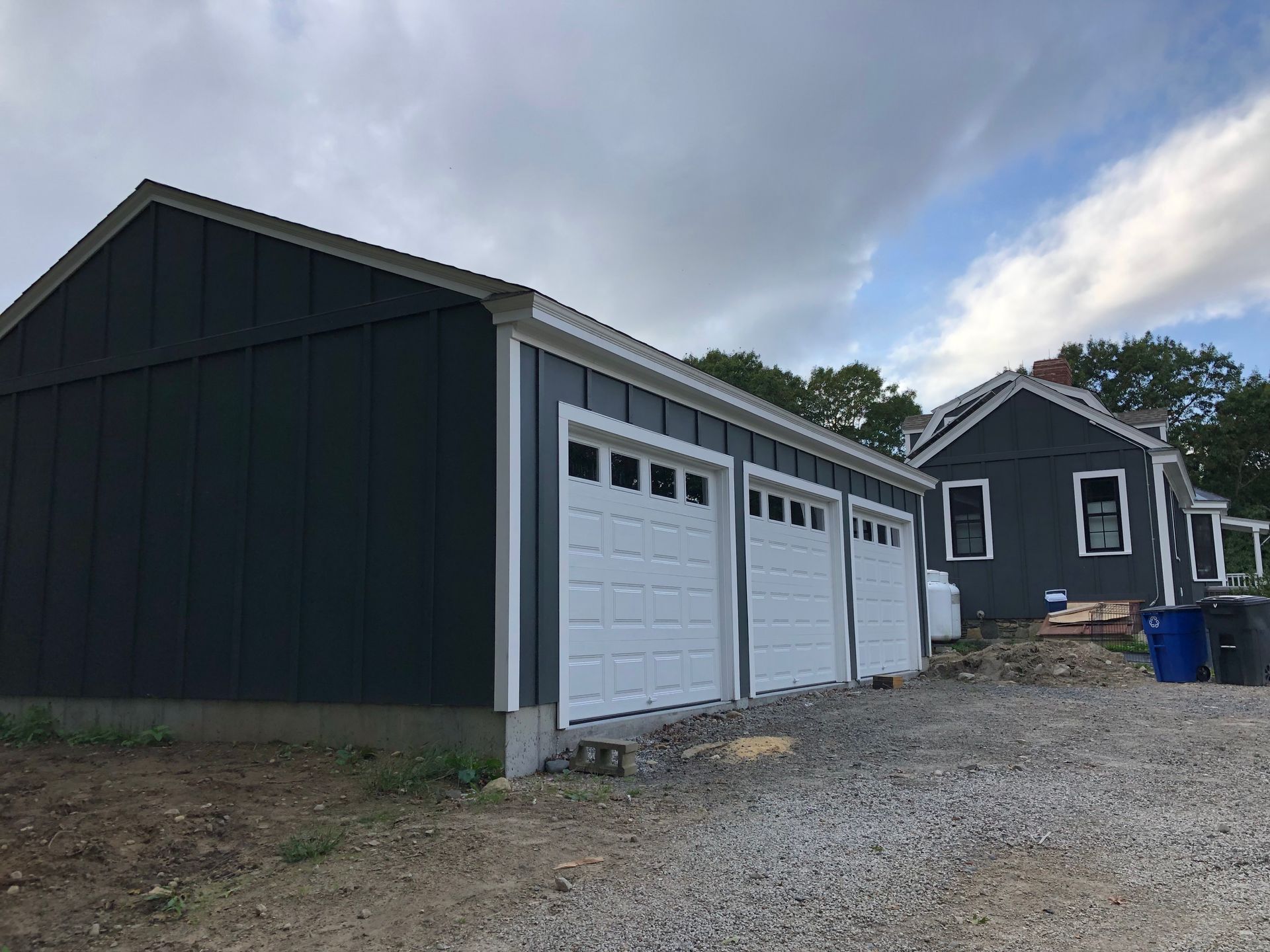 A garage with three white garage doors is next to a house.