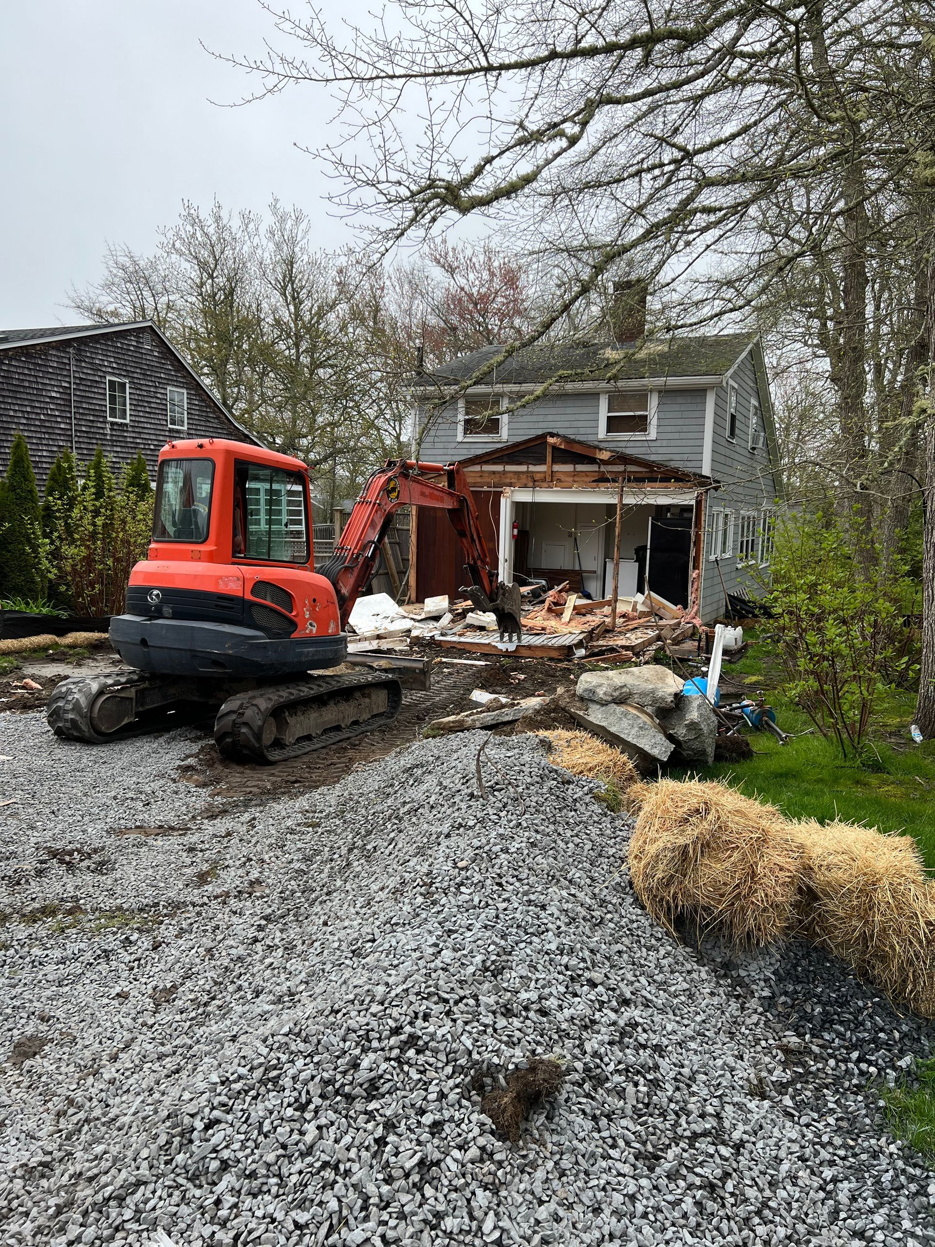 An excavator is demolishing a house in a gravel lot.