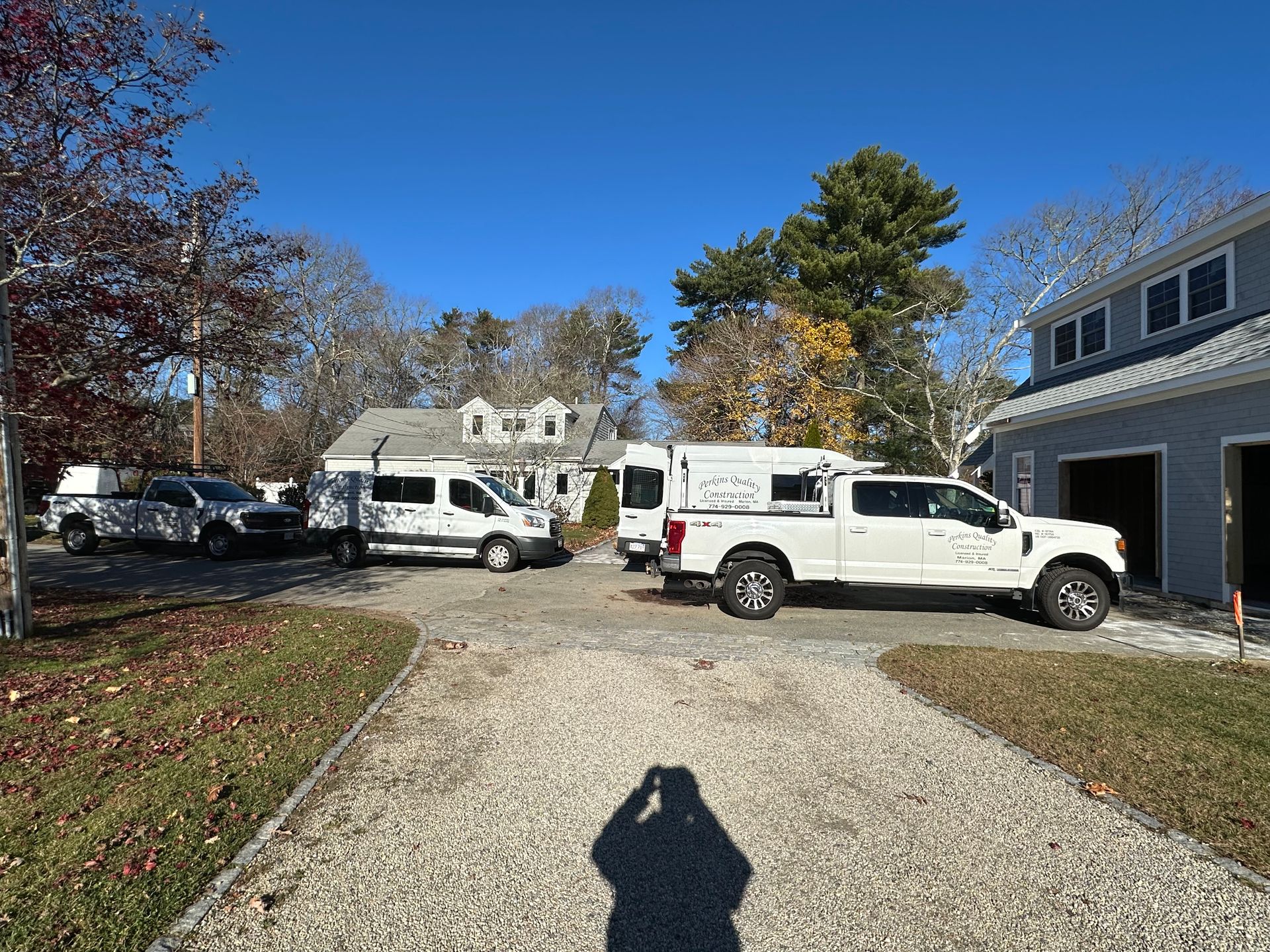 Three white trucks are parked in front of a house on a gravel driveway.