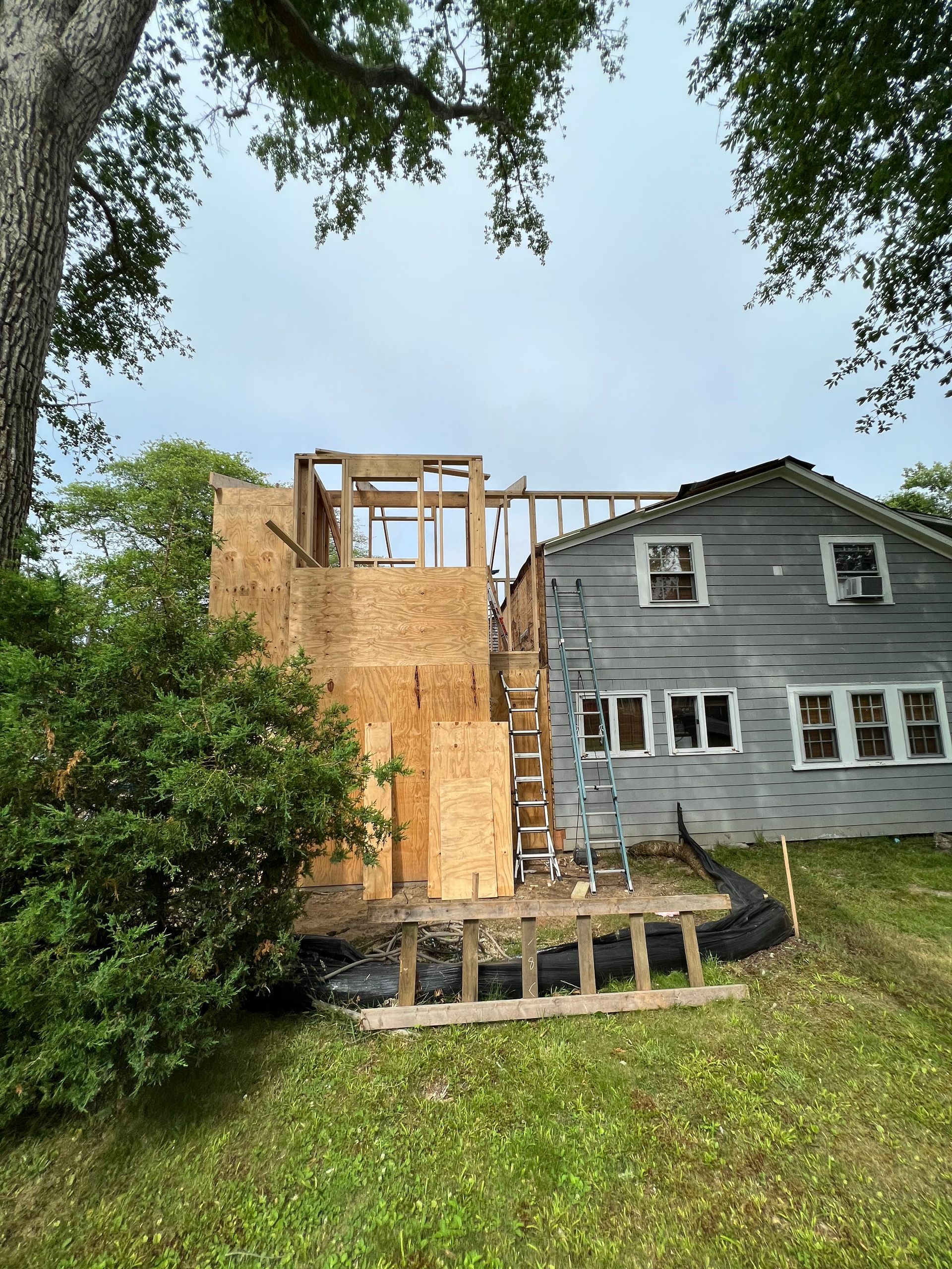 A house is being remodeled with a ladder in the backyard.