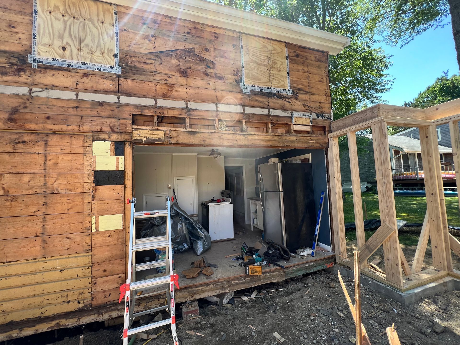 A ladder is sitting in front of a wooden house that is being remodeled.