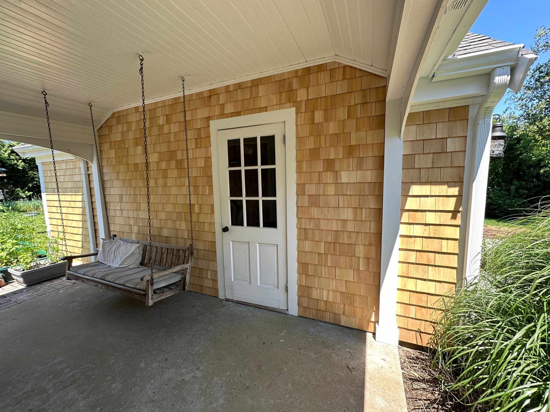 A porch with a swing hanging from the ceiling and a door.