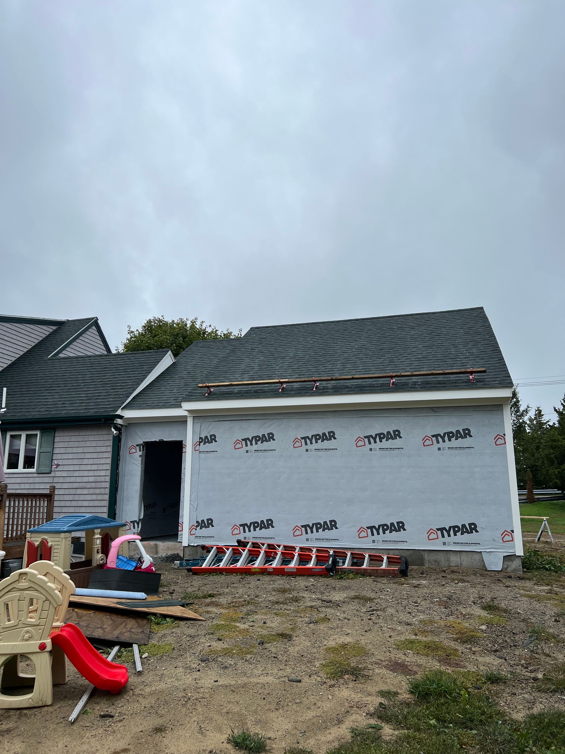 A house with a roof that is being built and a playground in front of it.