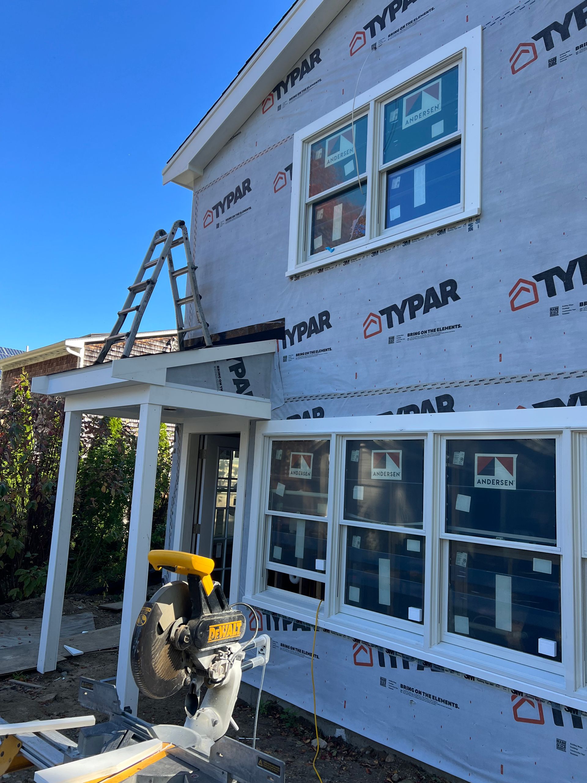 A person is using a miter saw on the side of a house.