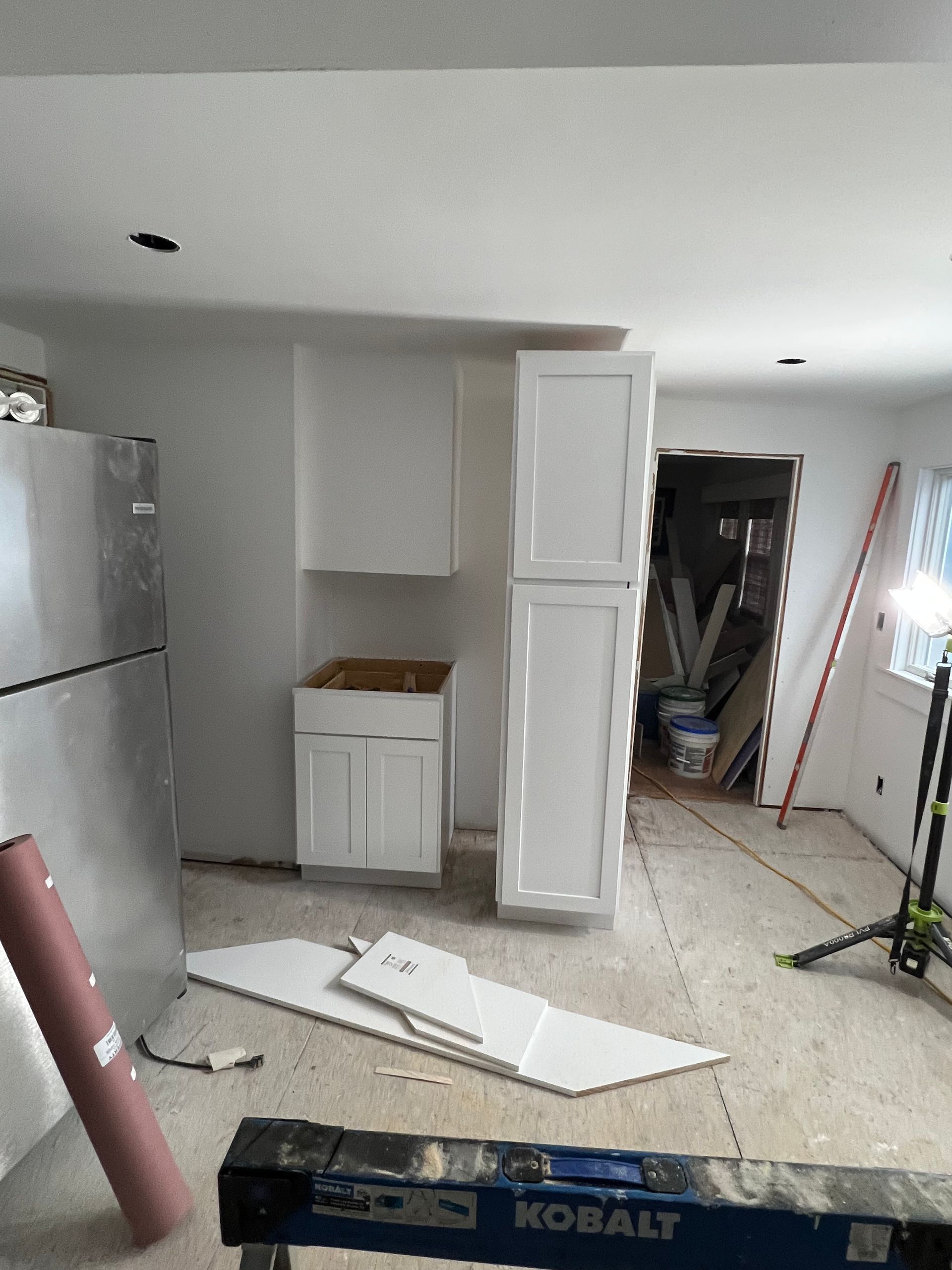 A kitchen is being remodeled with white cabinets and a refrigerator.