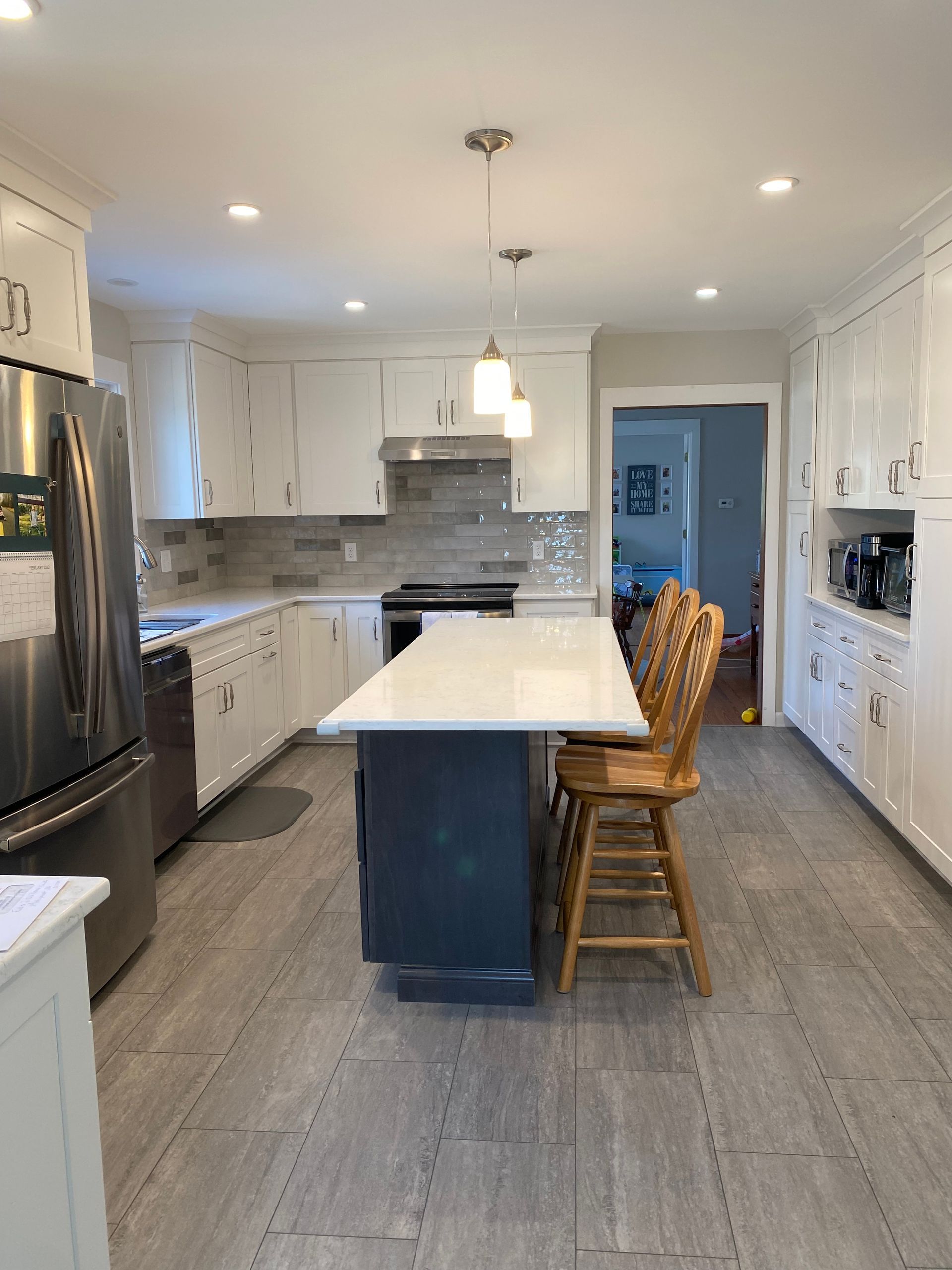 A kitchen with white cabinets , stainless steel appliances , a large island , and wooden chairs.