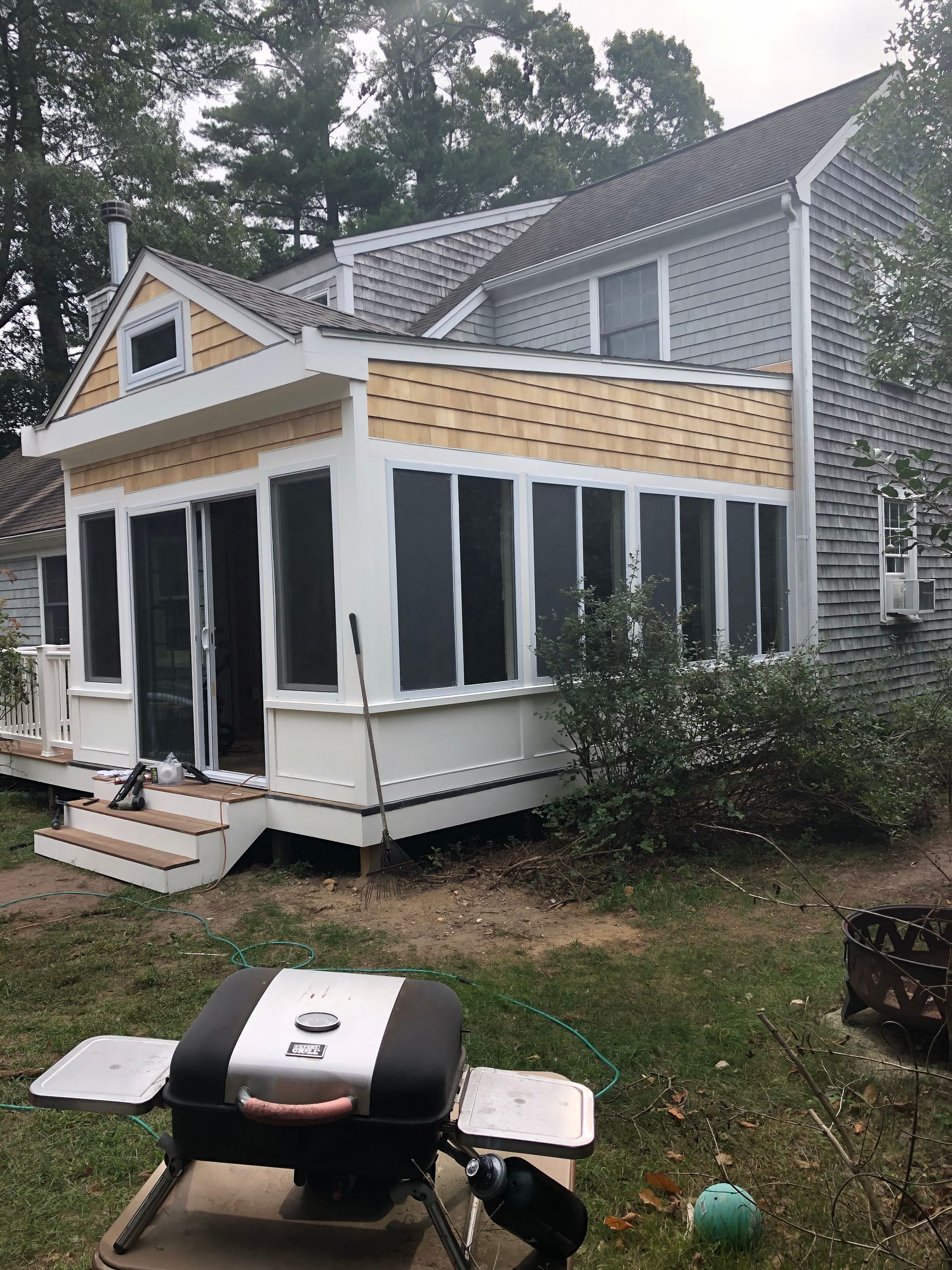 A house with a screened in porch and a grill in front of it.