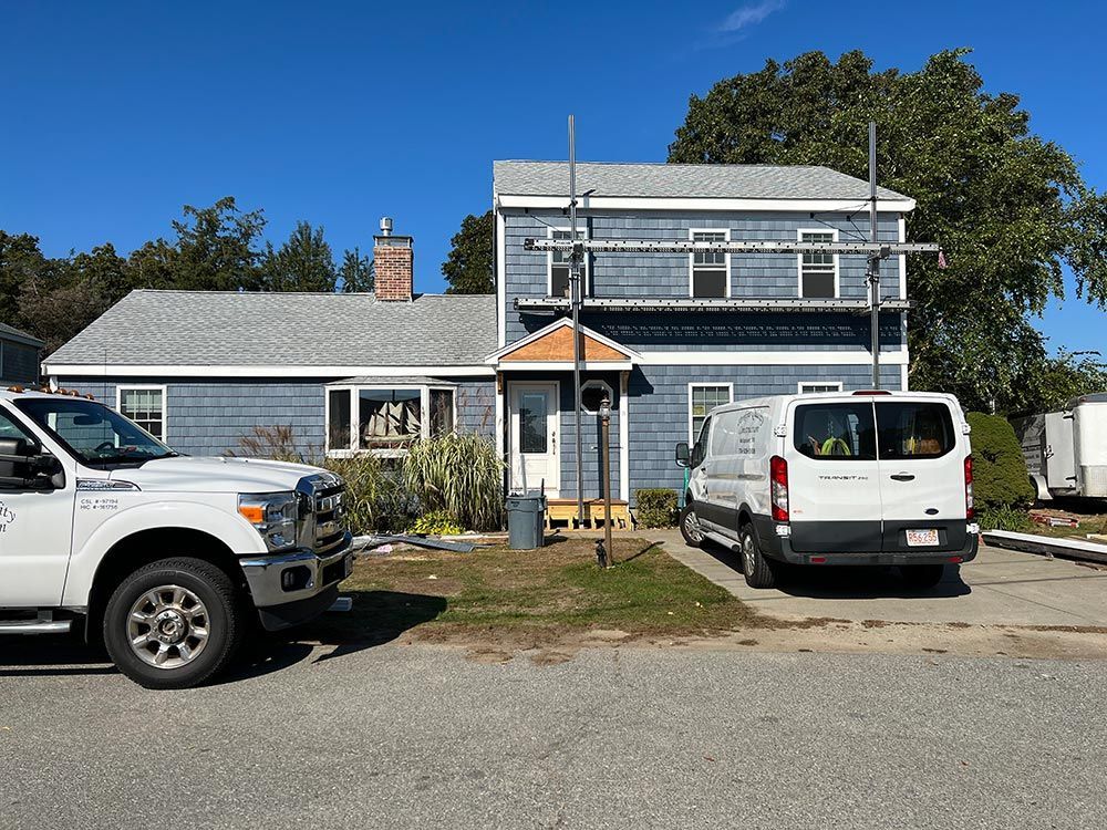 Two white vans are parked in front of a blue house.