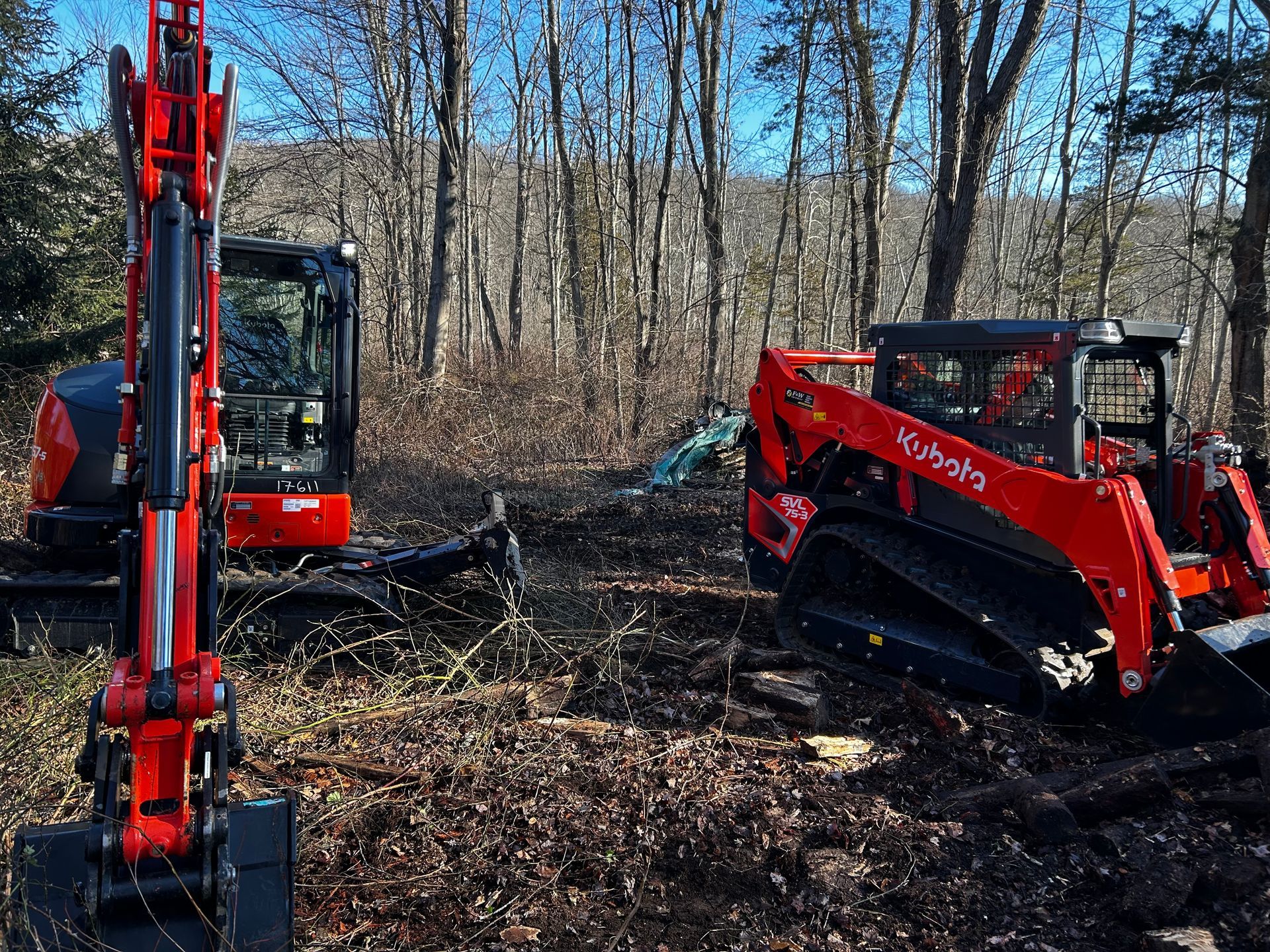 Two tractors are parked next to each other in the woods.