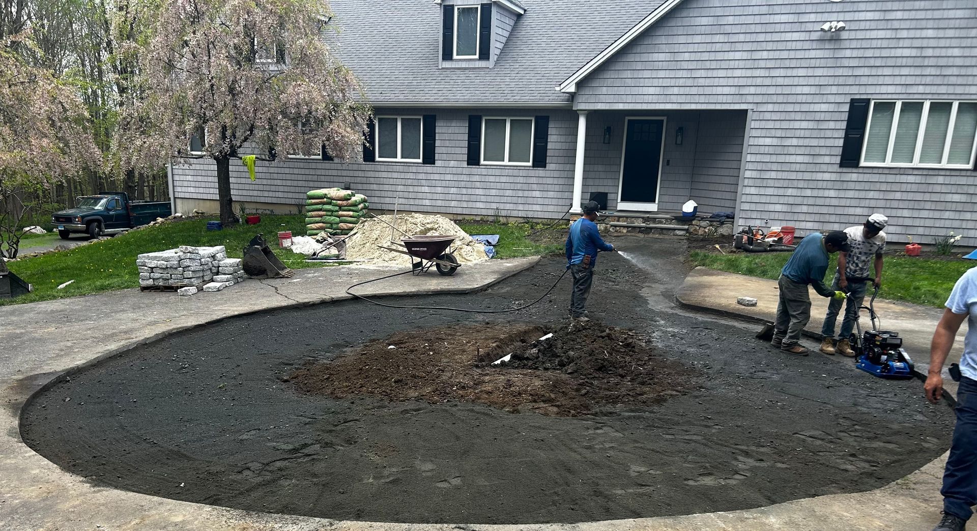 A group of people are working on a driveway in front of a house.
