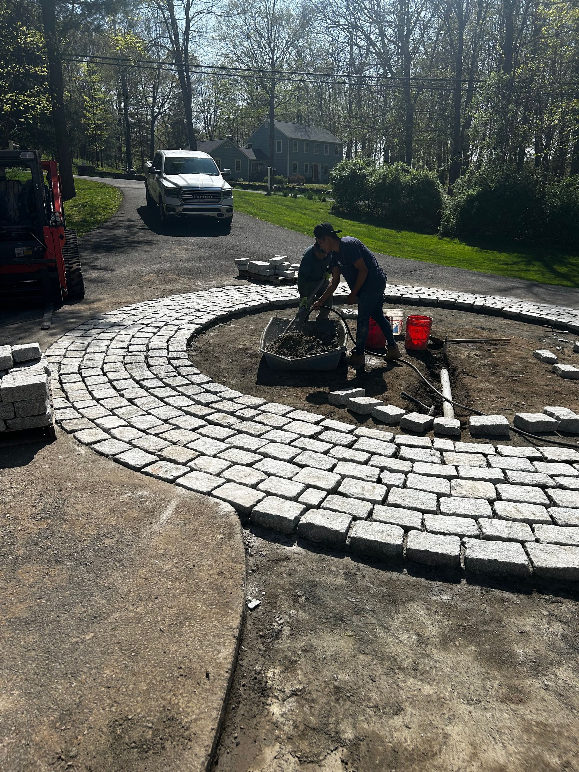 A man is working on a brick walkway in a driveway.