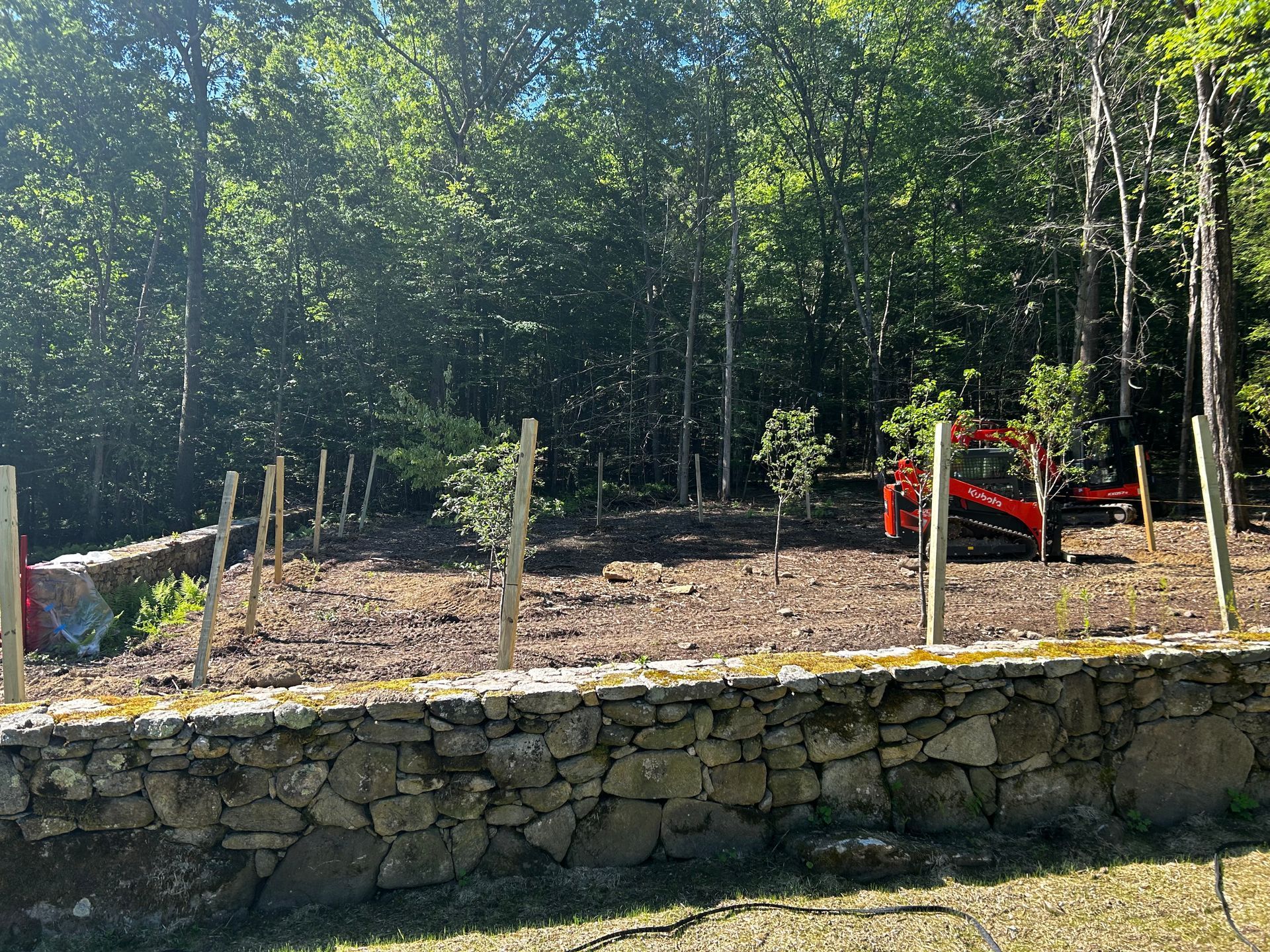 A stone wall surrounds a dirt field with trees in the background.