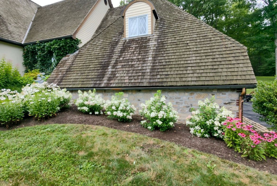 A house with a roof that is covered in shingles and flowers in front of it.