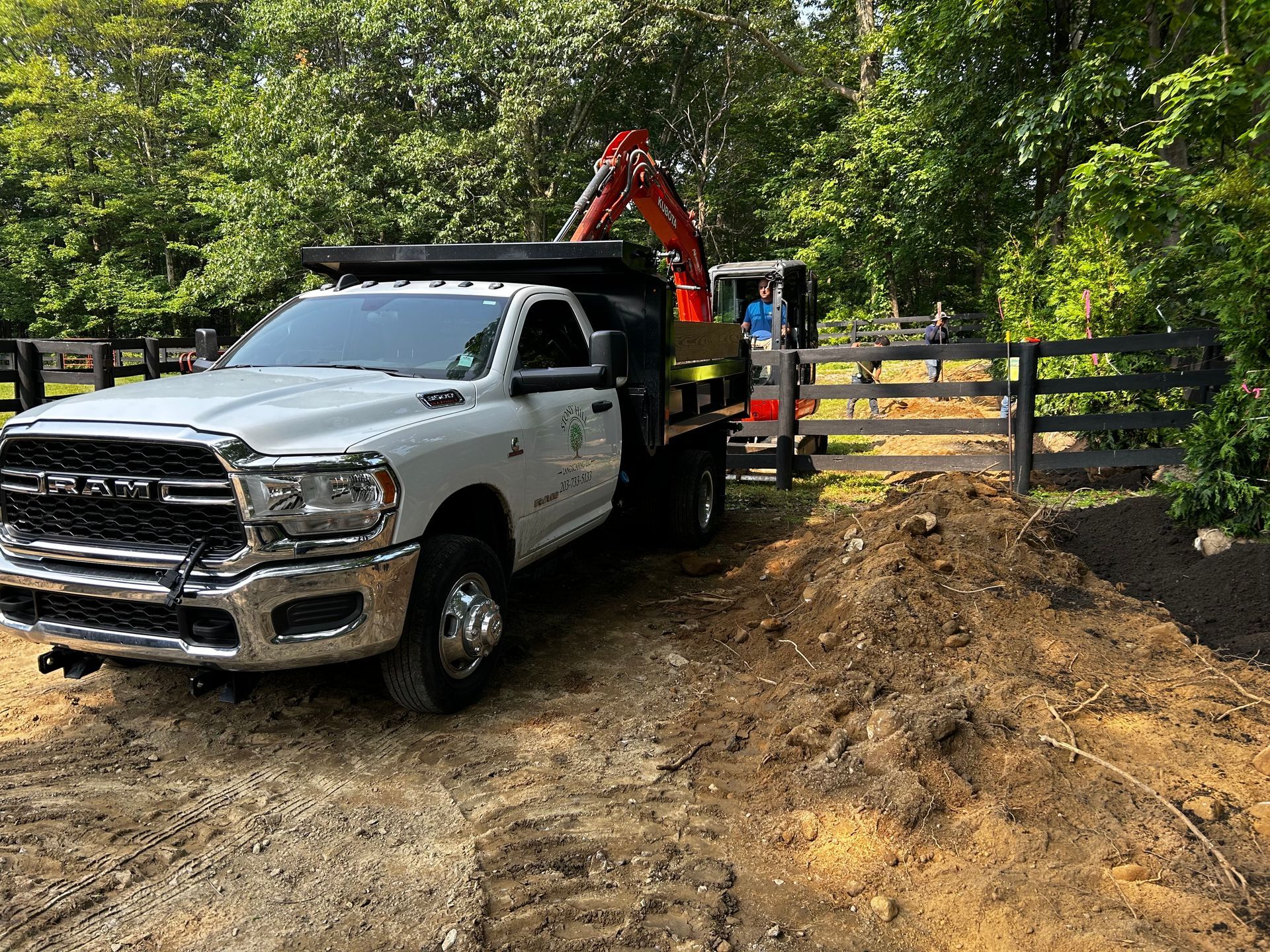 A dump truck is parked in the dirt next to a fence.