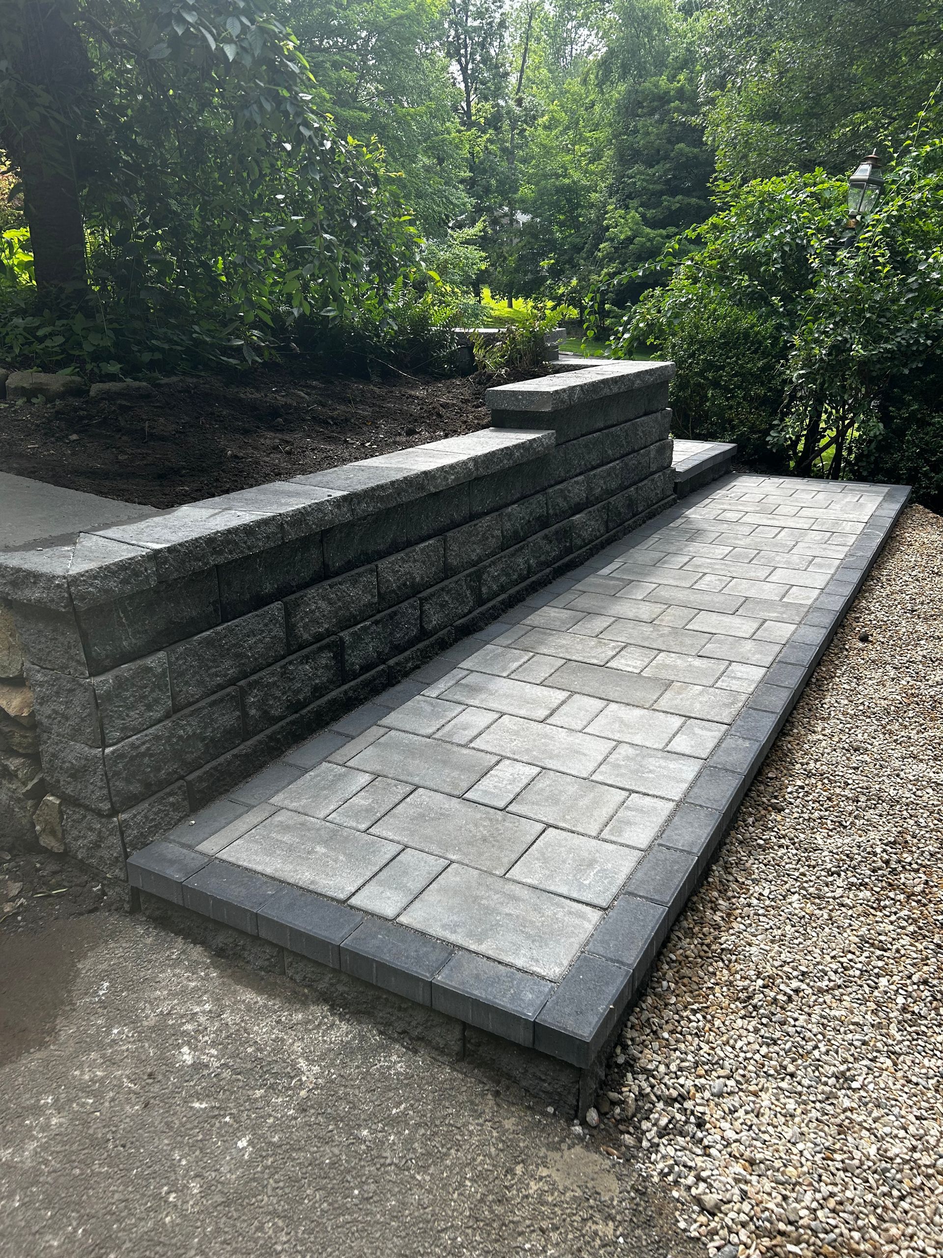 A brick walkway leading to a stone wall in a garden.