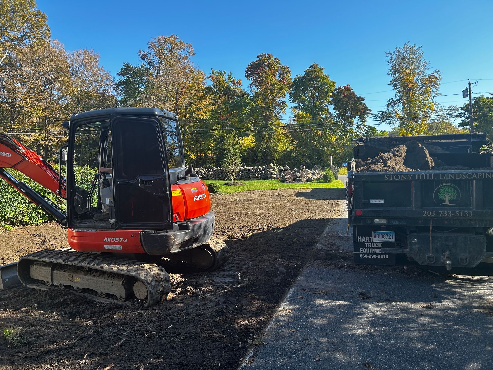 A red excavator is parked next to a dumpster in a dirt lot.