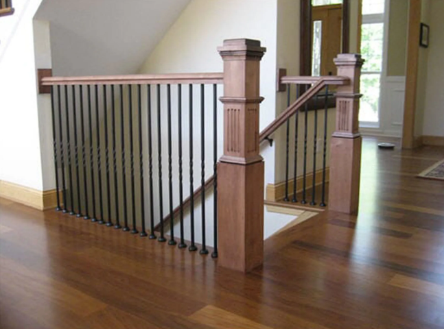 Wooden staircase railing with black vertical bars, in a well-lit home.