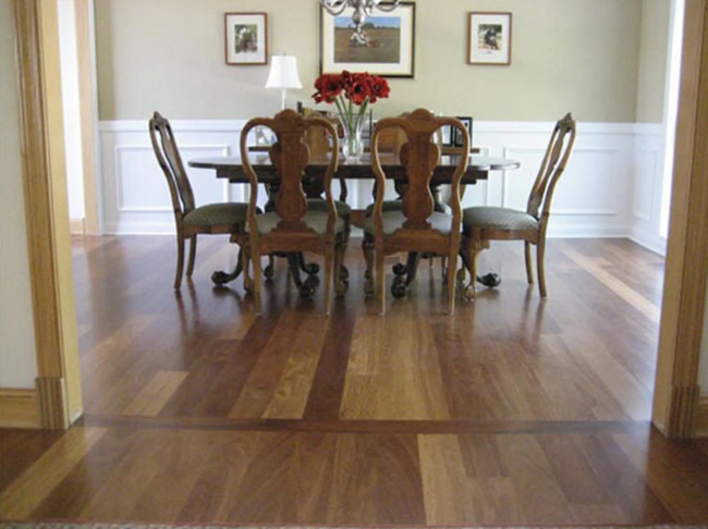 Dining room with hardwood floor, round table, chairs, and artwork; a vase of flowers is centered.