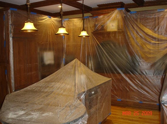 Interior room with wood paneling and furniture covered in plastic sheeting, prepared for renovation.