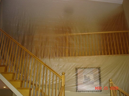 Staircase with plastic sheeting covering walls and a painting.