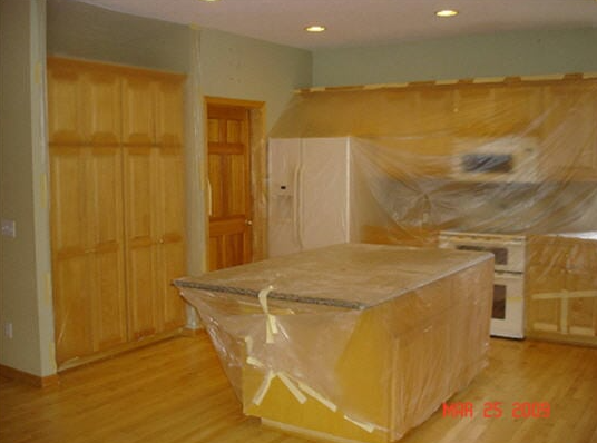 Kitchen with cabinets and island covered in plastic for protection, walls are light green, hardwood floors.