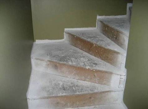 Curved wooden staircase with cement coating between green walls.