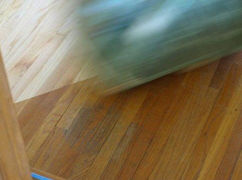 Blurred view of a green object rolling on a hardwood floor.