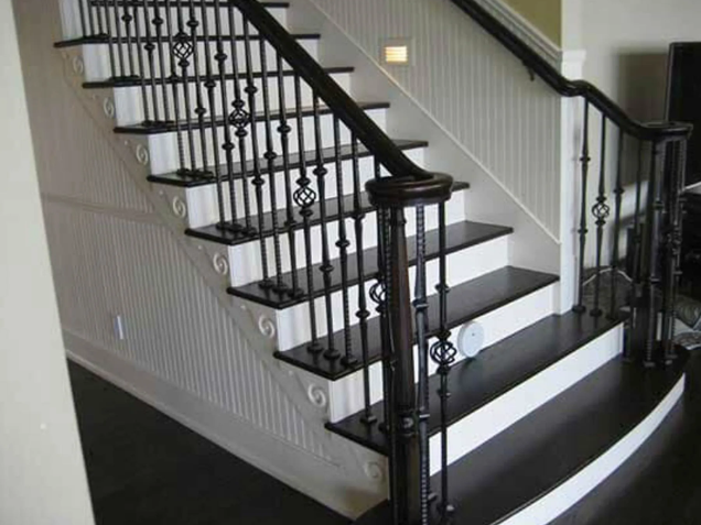 Staircase with black treads, white risers, black wrought iron railing, and dark wooden handrails.