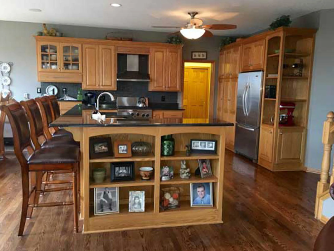 A kitchen with wooden cabinets and island, stainless steel appliances, and wood flooring.