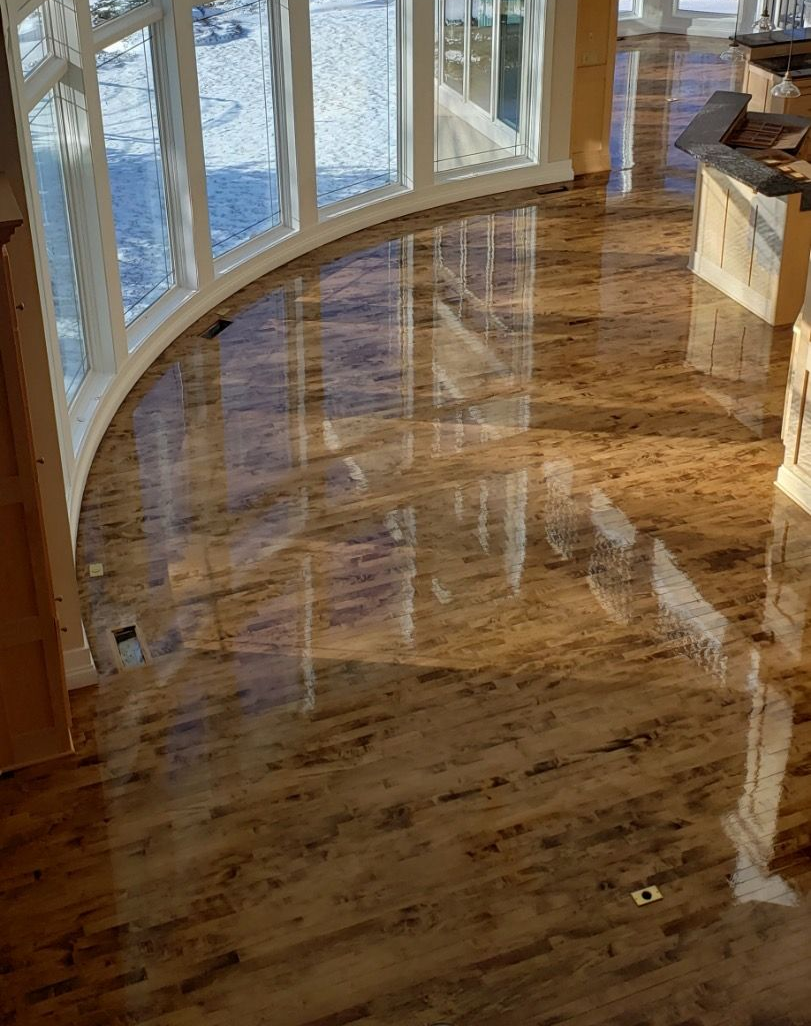 Glossy, wooden-look floor reflecting a bright, curved window with outdoor scenery.